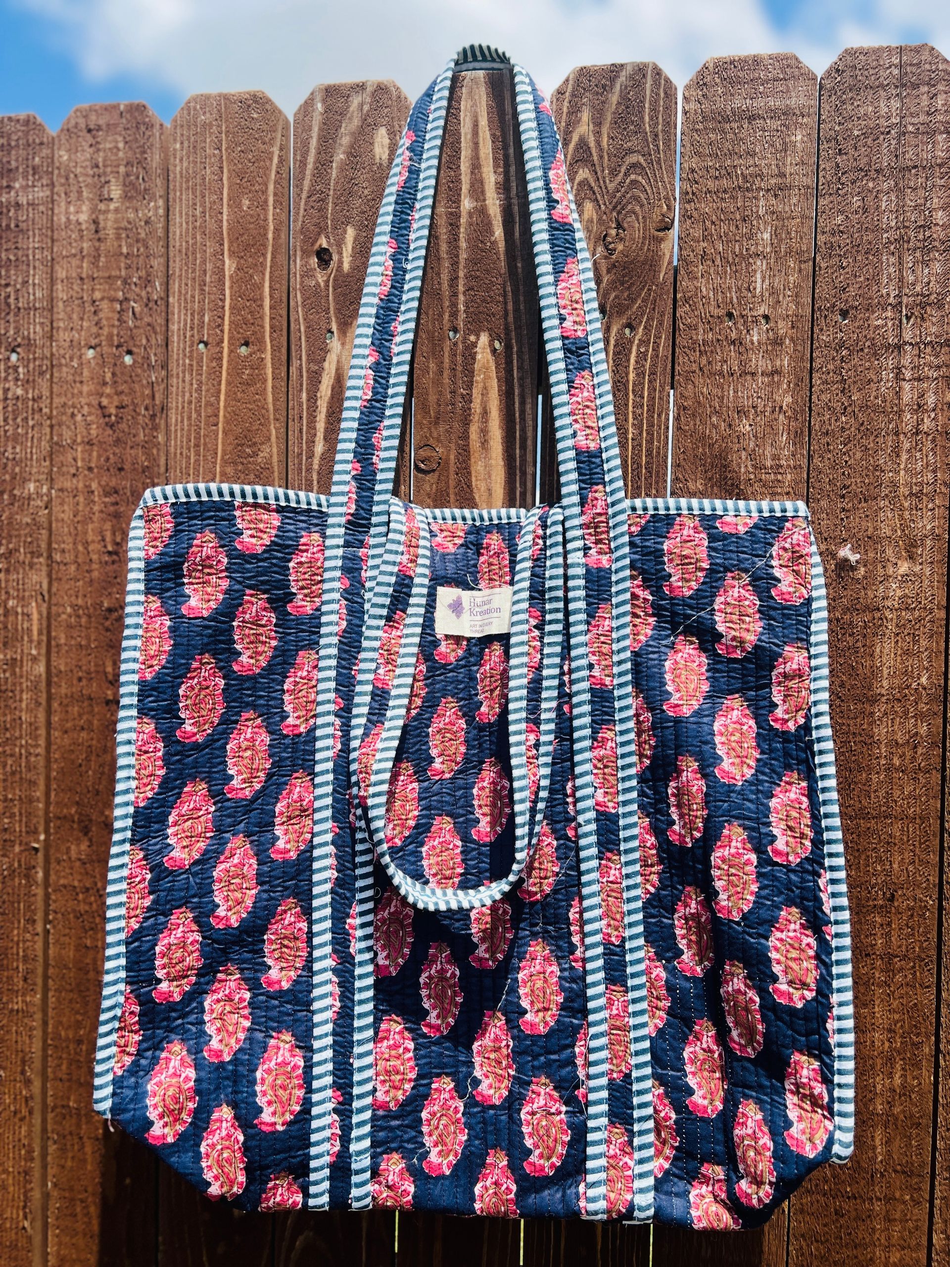 A blue and pink tote bag is hanging on a wooden fence