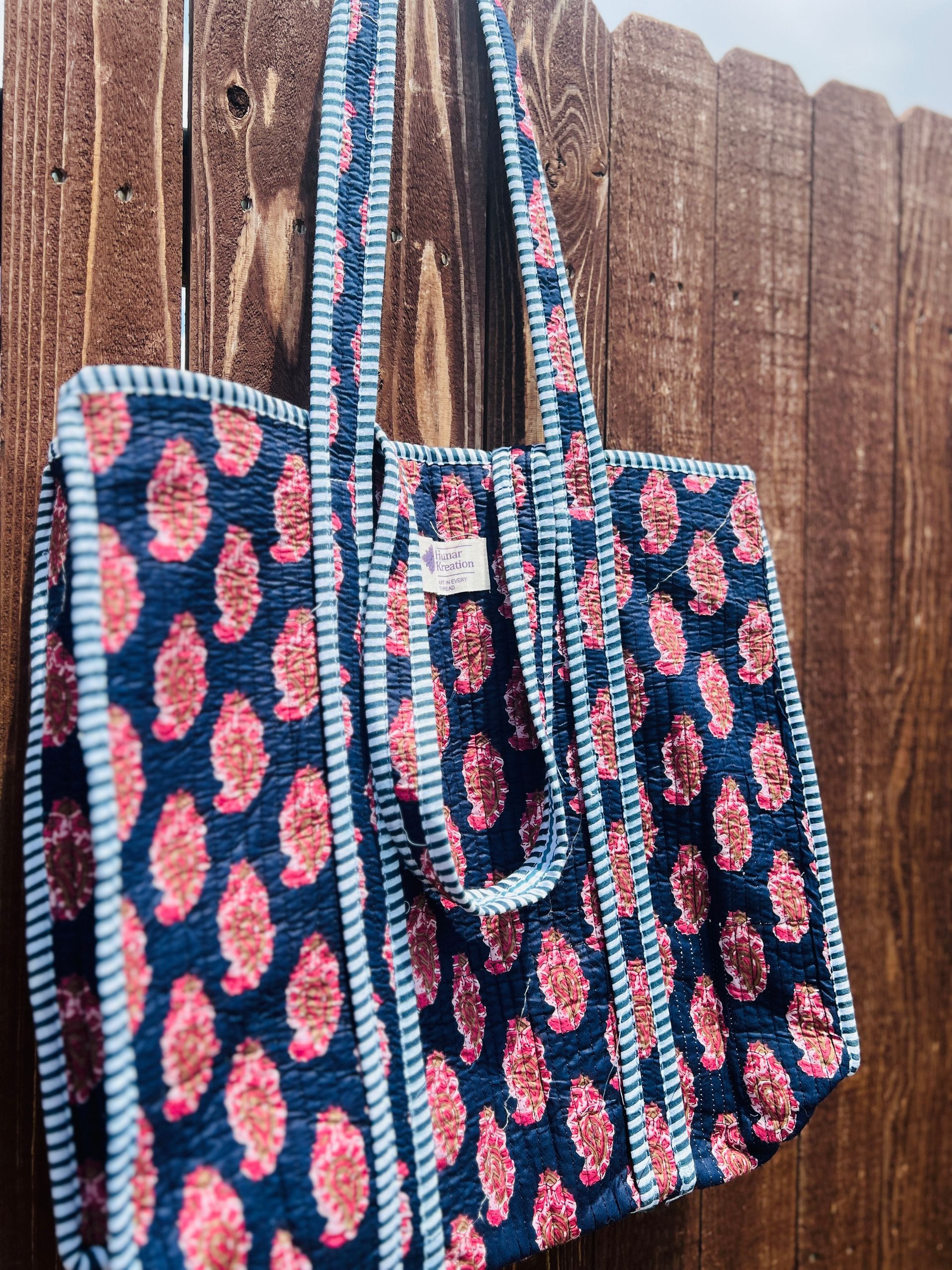 A blue and pink tote bag is hanging on a wooden fence