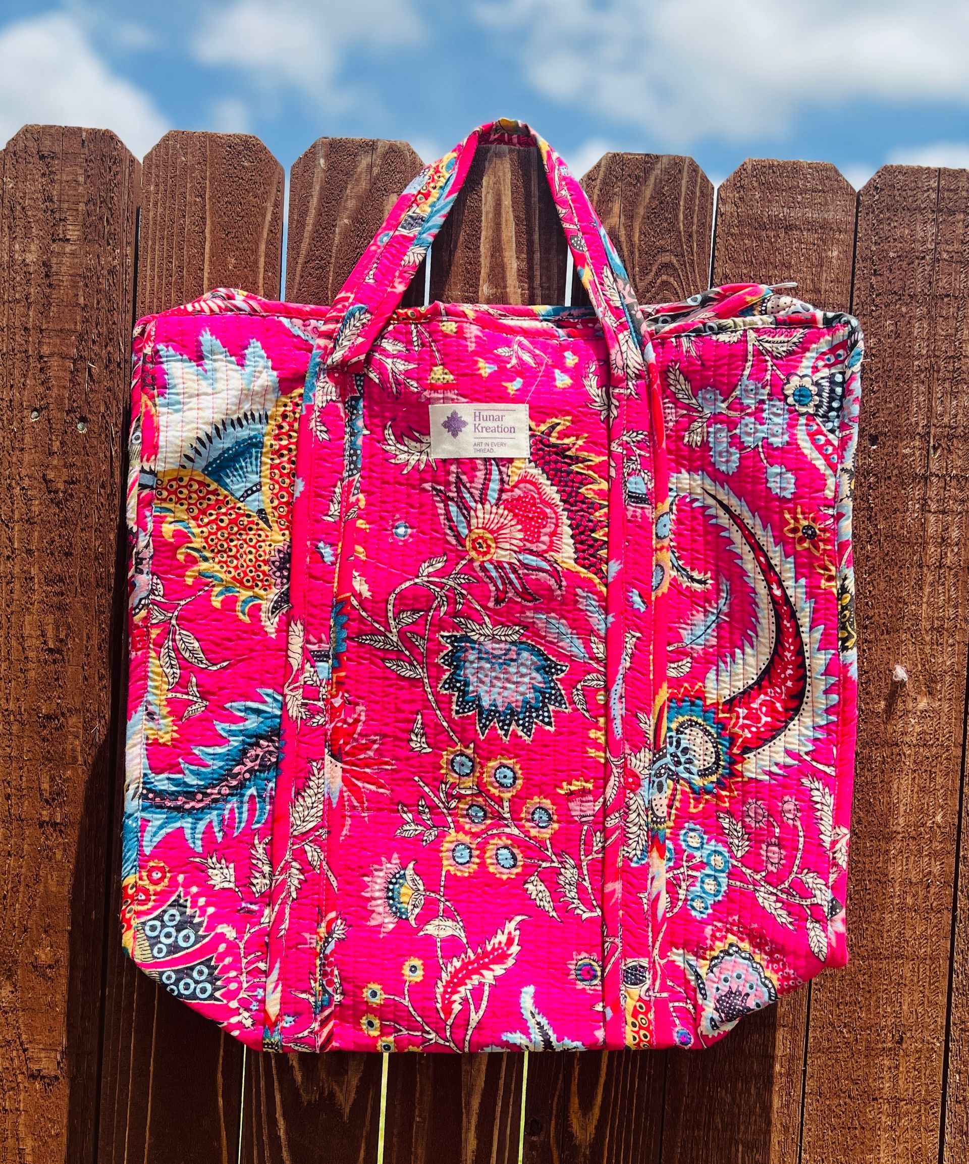 A pink paisley tote bag is hanging on a wooden fence