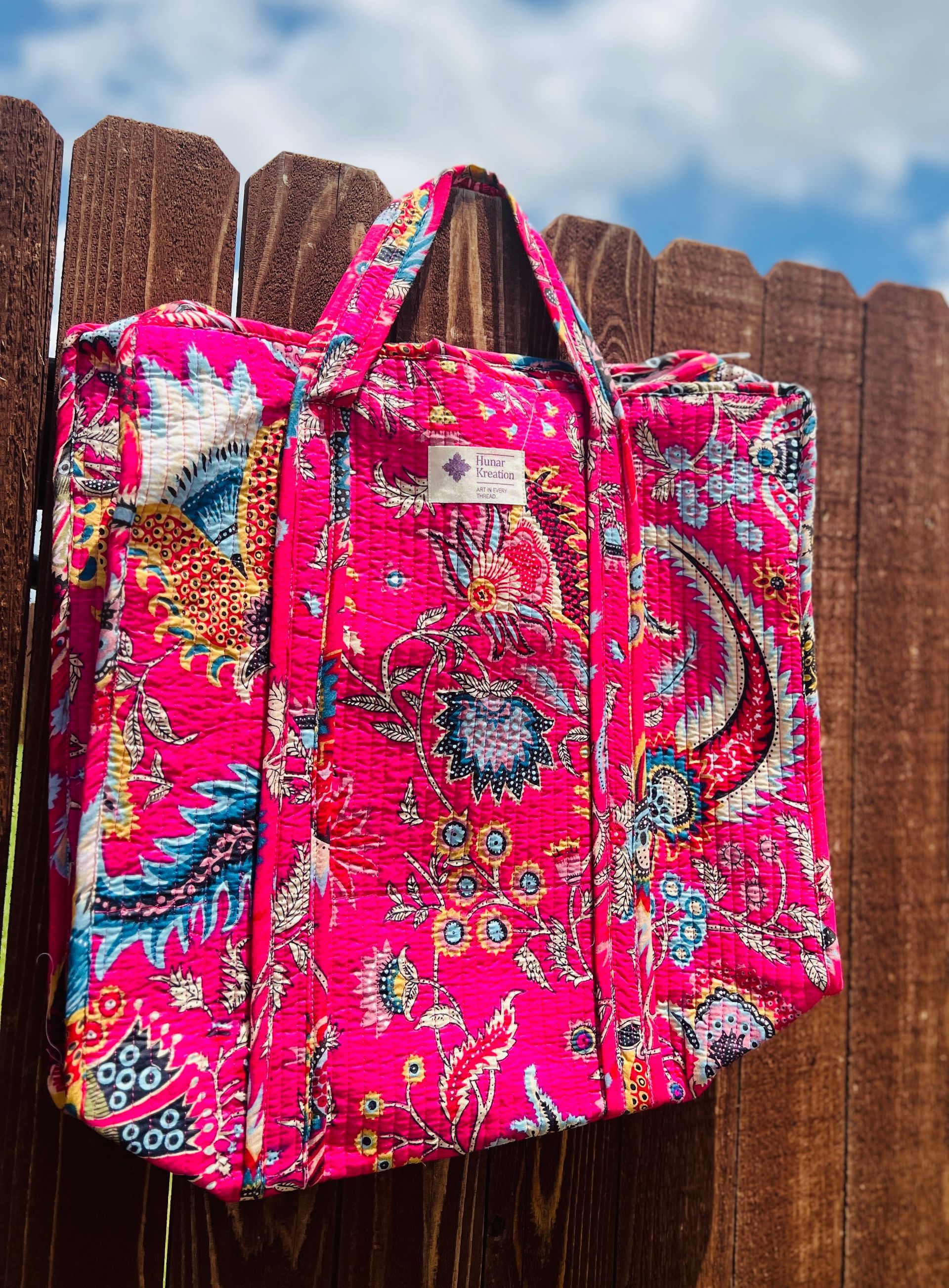 A pink paisley tote bag is hanging on a wooden fence