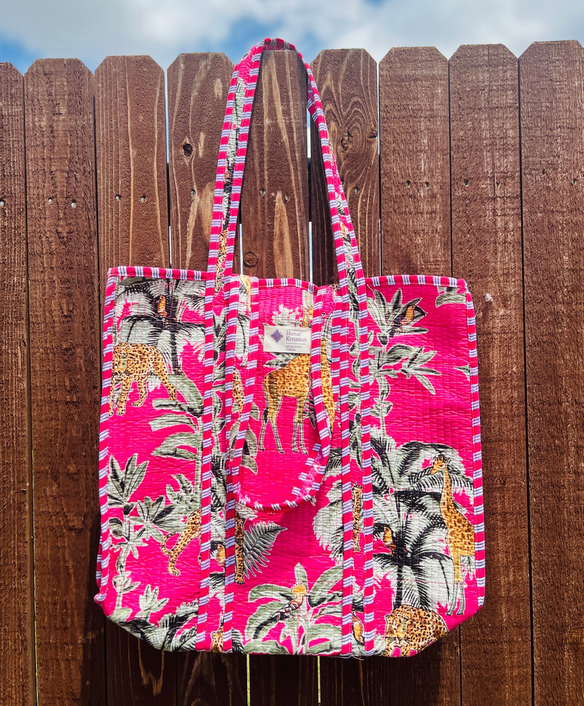 A pink tote bag is hanging on a wooden fence