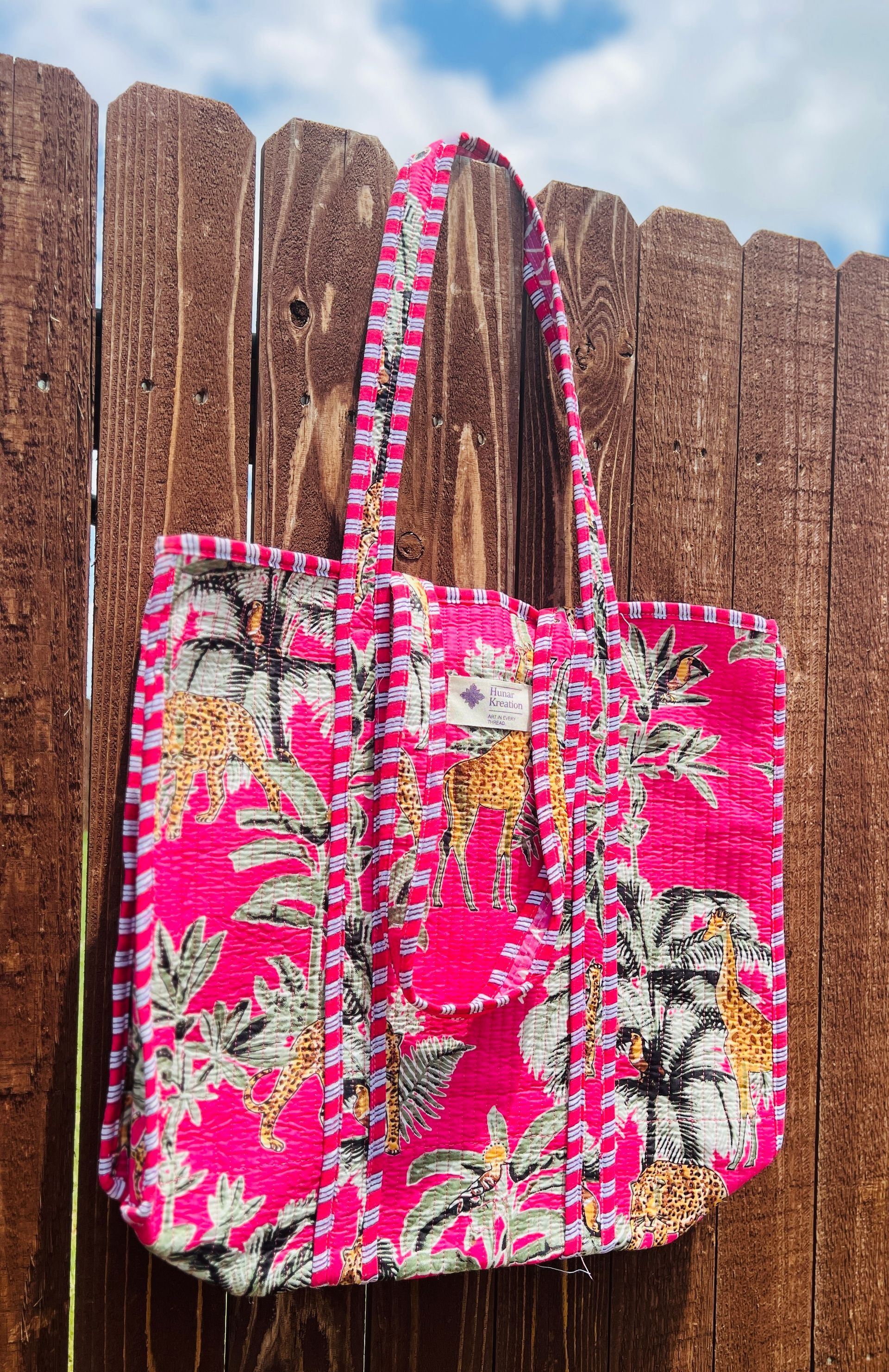 A pink tote bag is hanging on a wooden fence