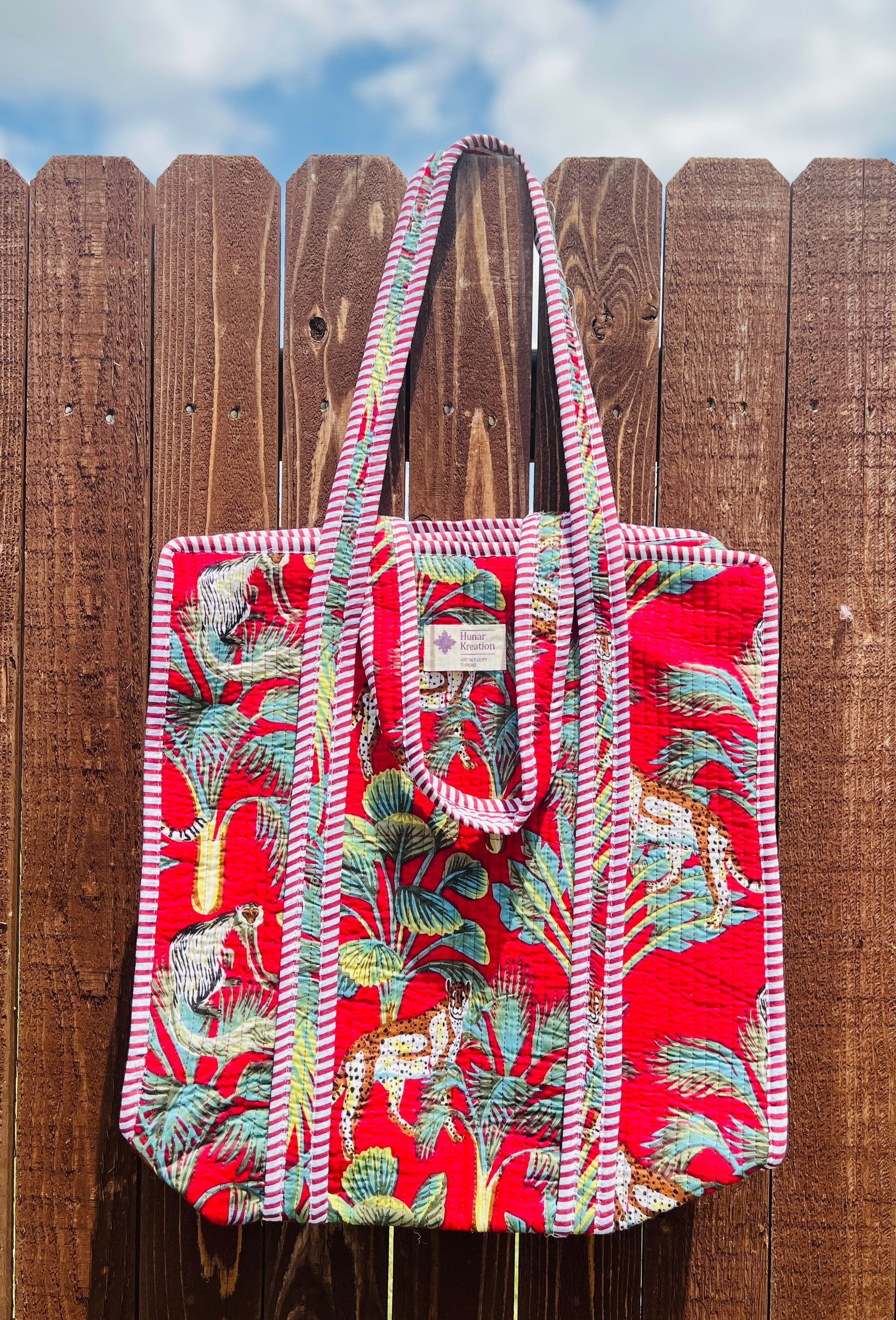 A red tote bag is hanging on a wooden fence.