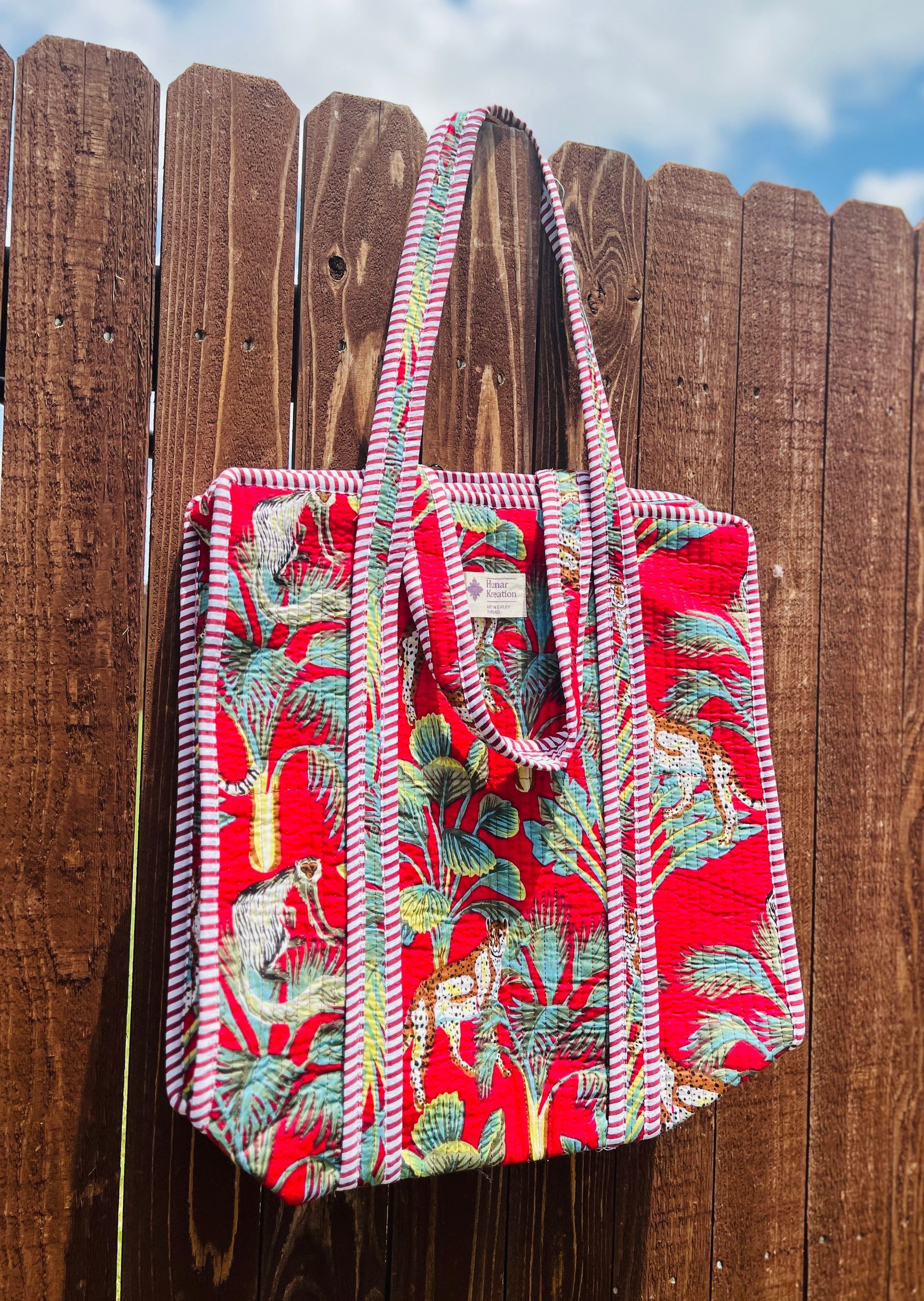A red tote bag is hanging on a wooden fence.