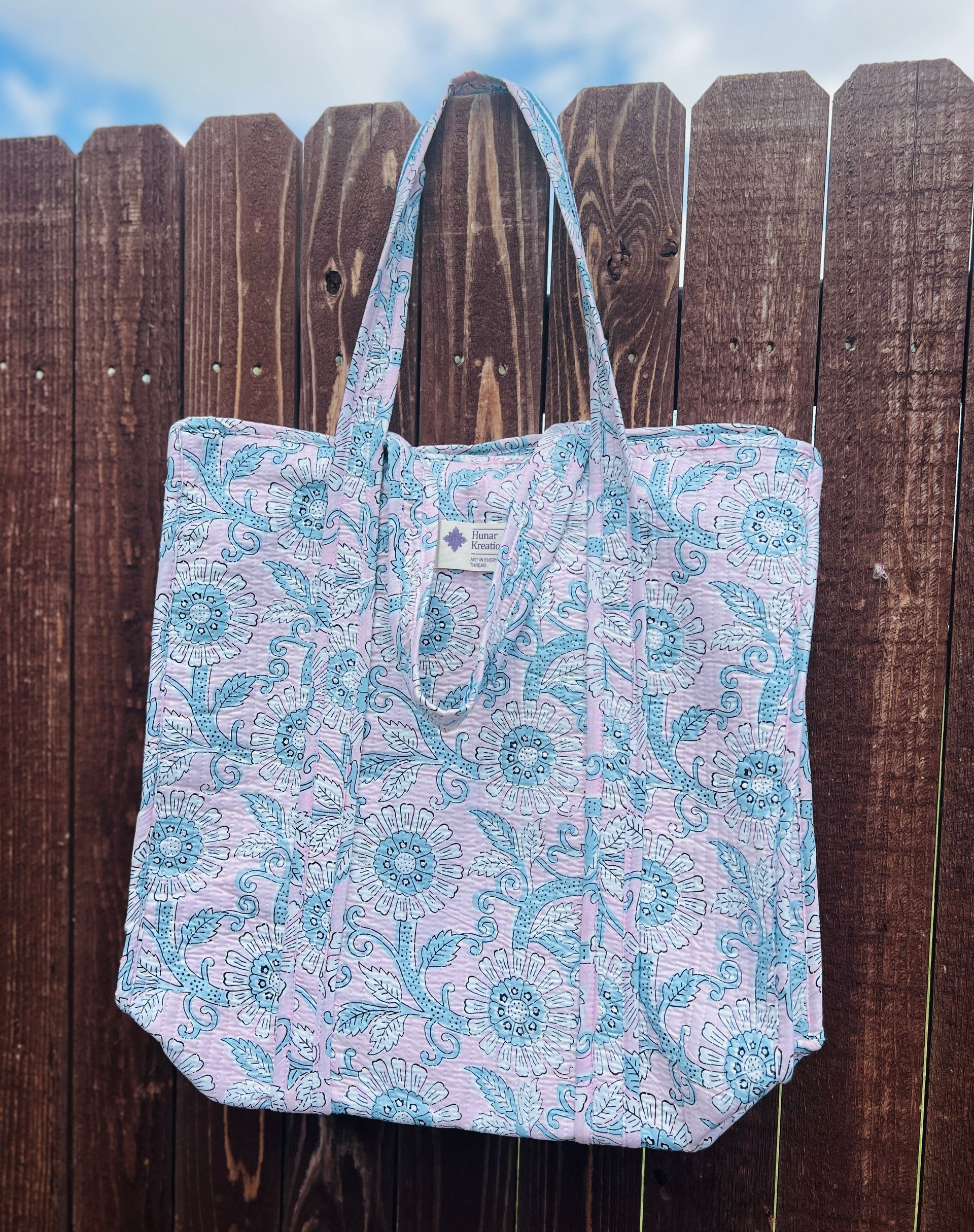 A tote bag is hanging on a wooden fence.