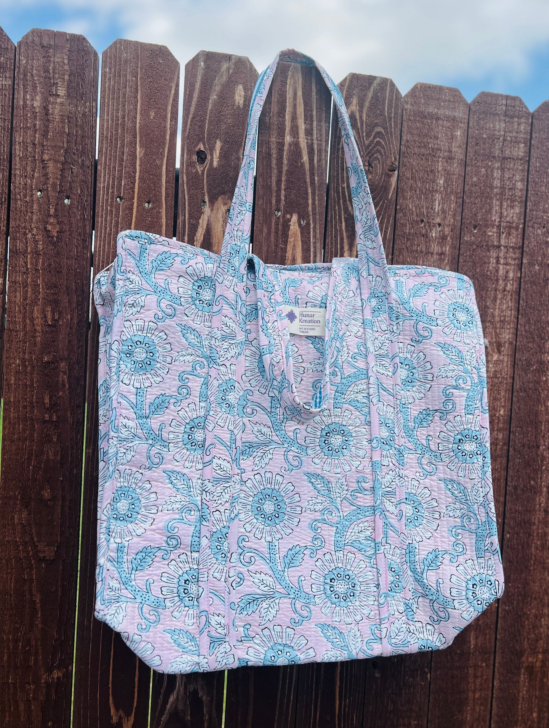 A tote bag is hanging on a wooden fence.