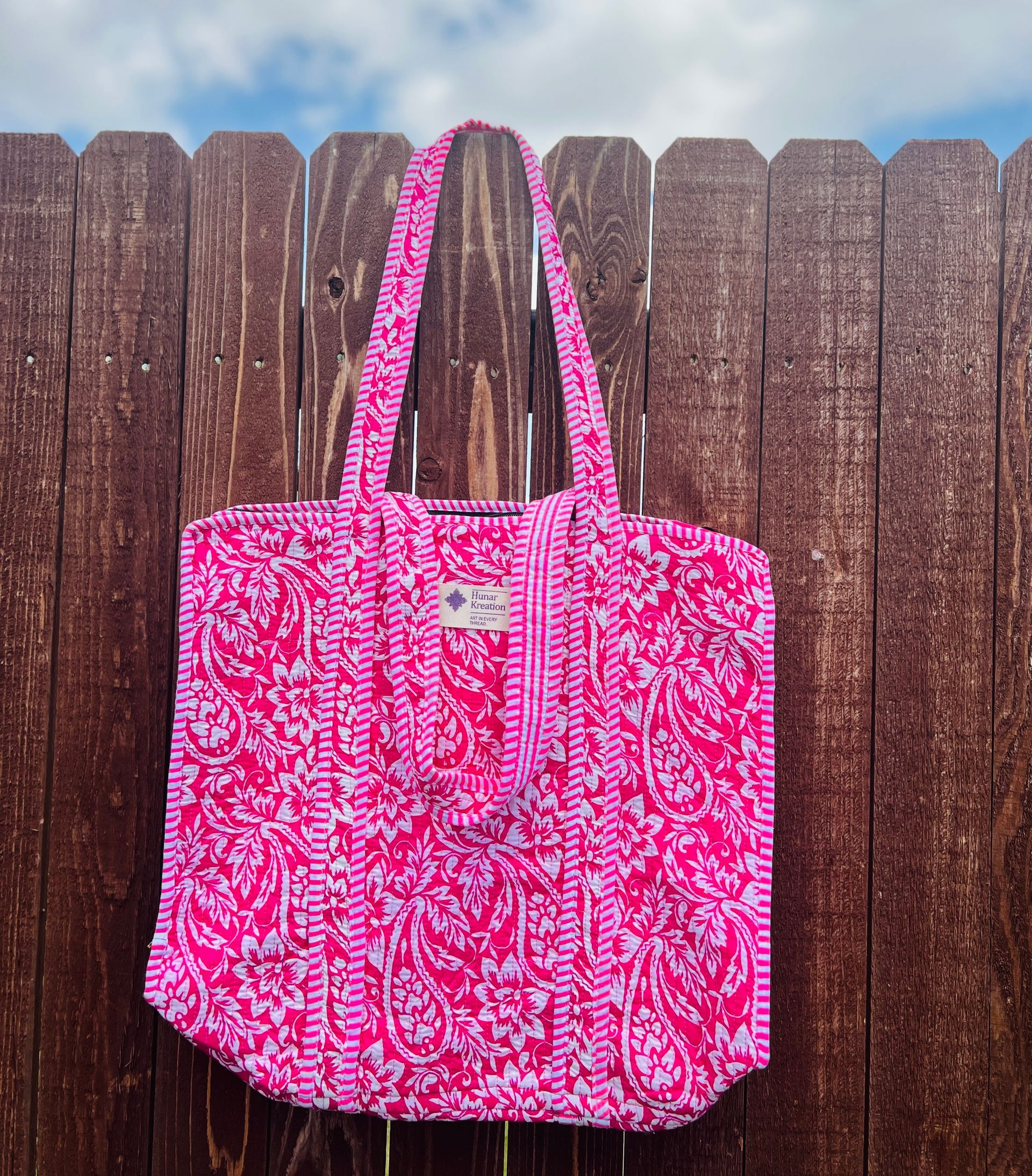 A pink tote bag is hanging on a wooden fence
