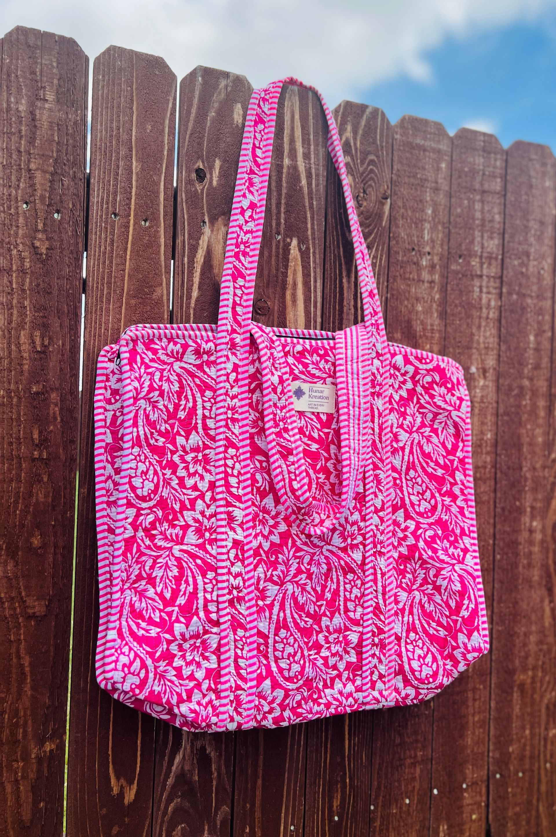 A pink tote bag is hanging on a wooden fence