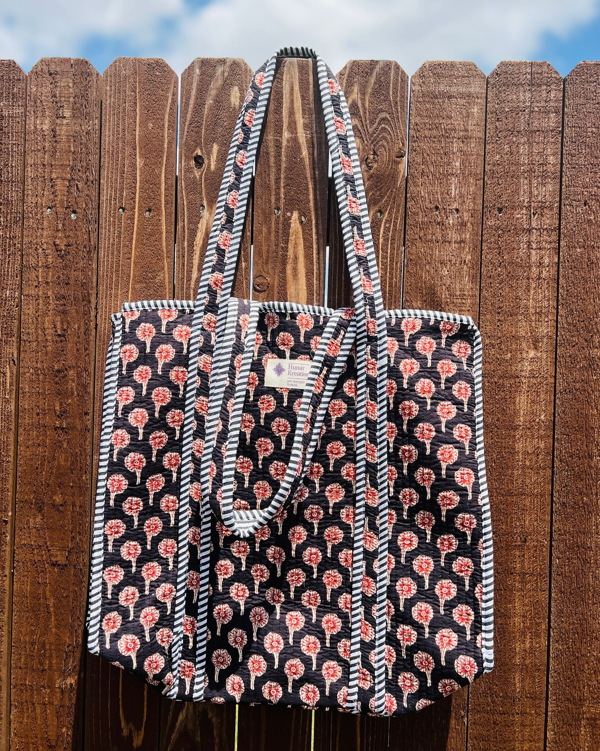 A black and red tote bag is hanging on a wooden fence