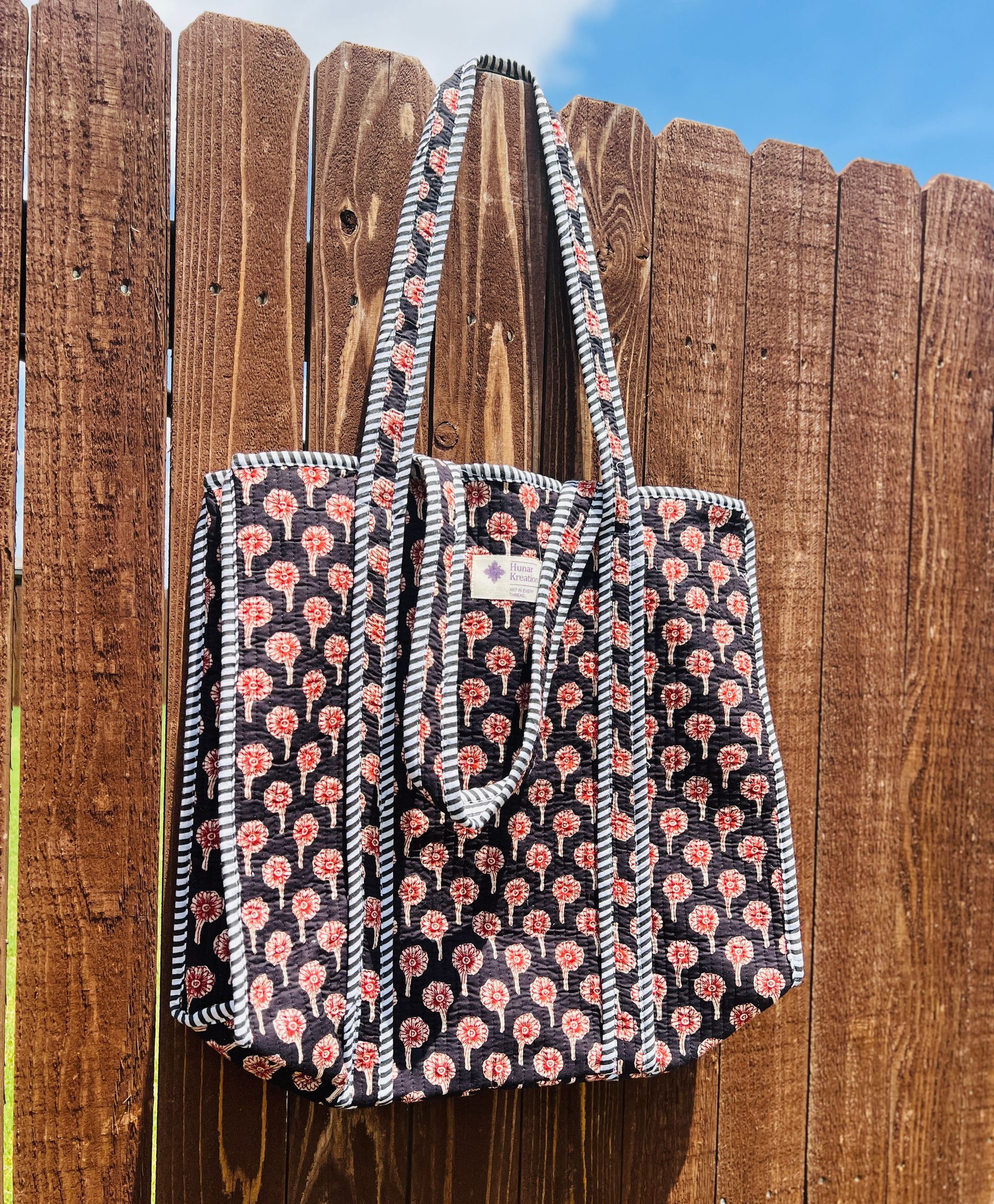 A black and red tote bag is hanging on a wooden fence