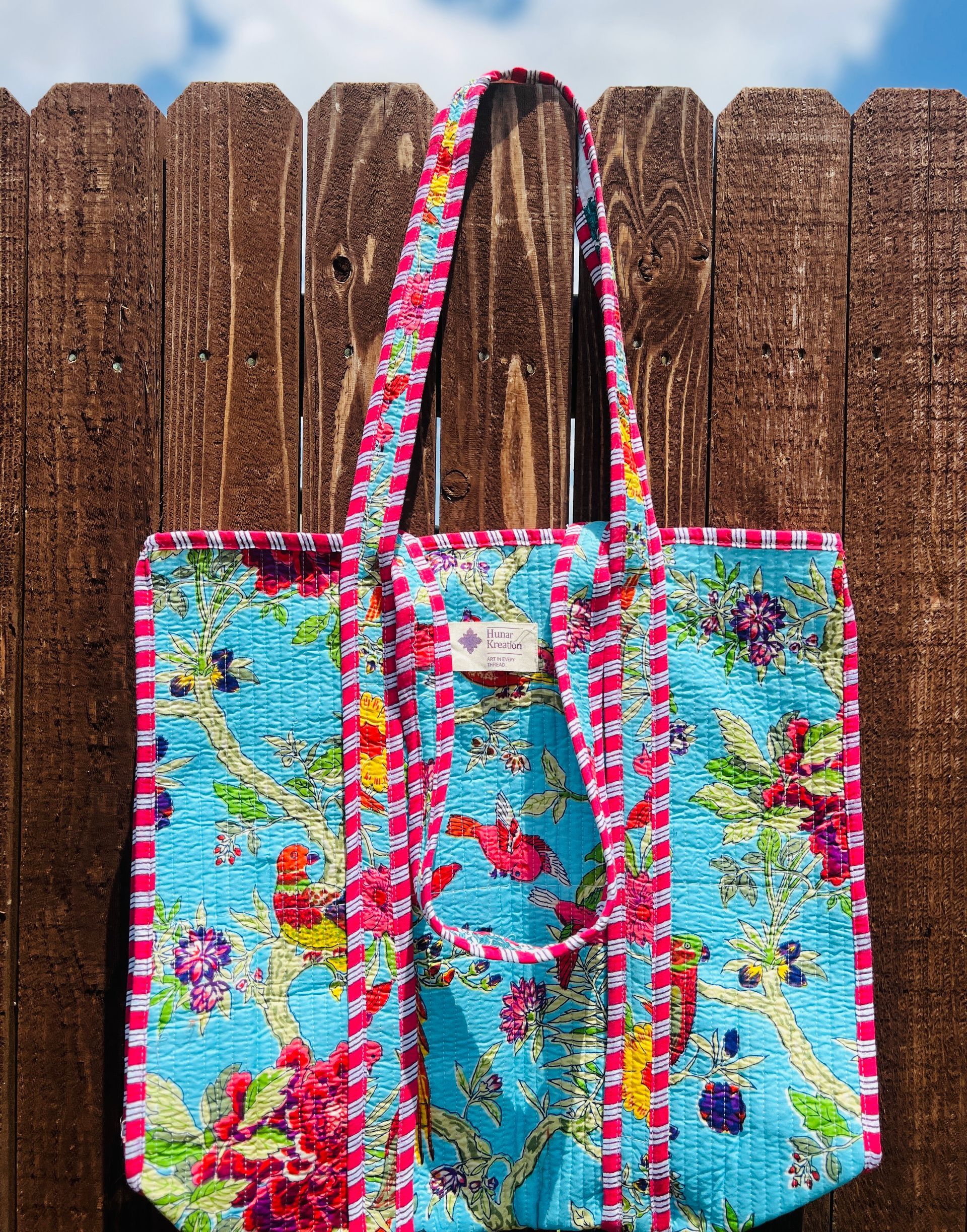 A colorful tote bag is hanging on a wooden fence.