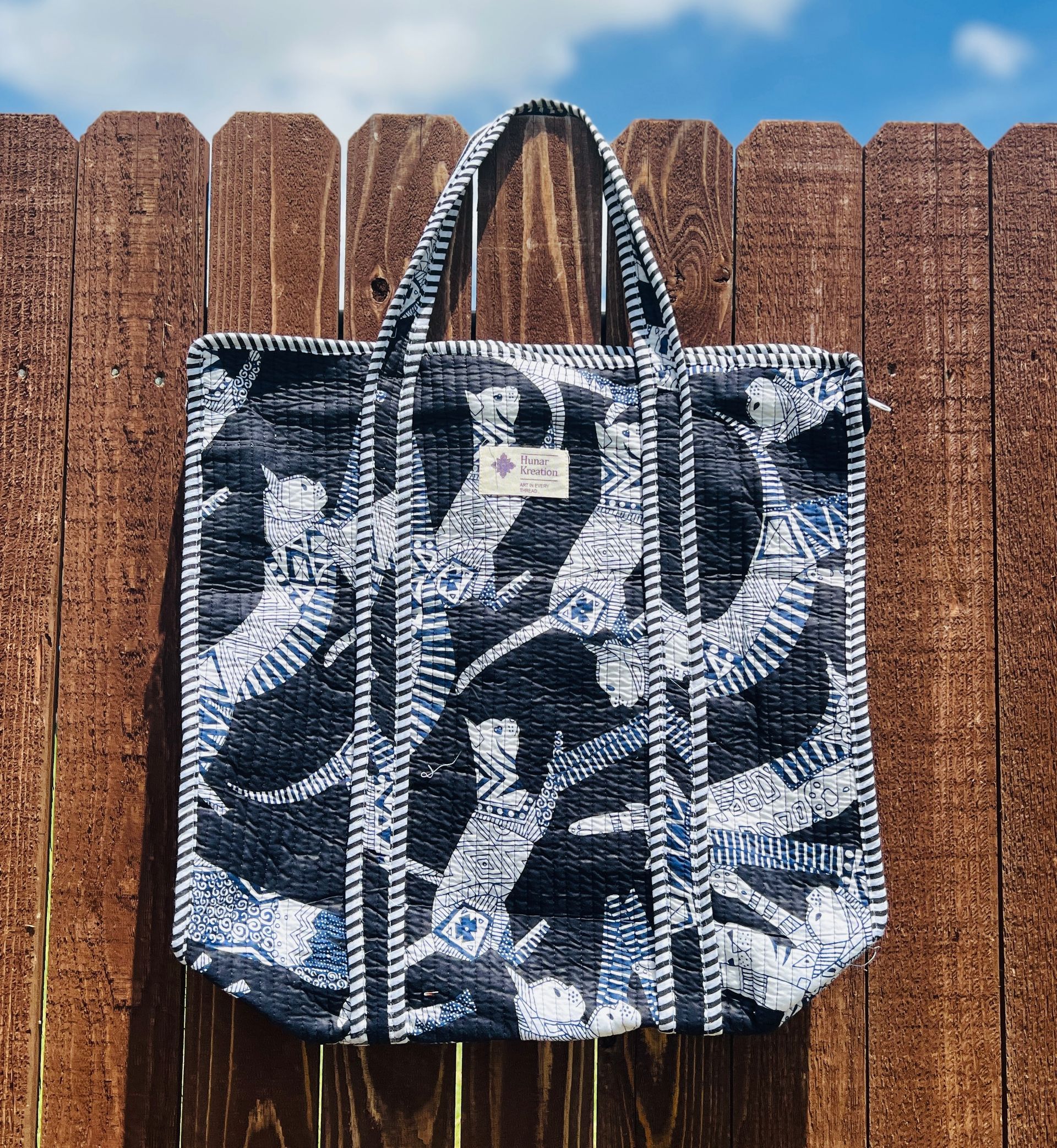 A black and white tote bag is hanging on a wooden fence.