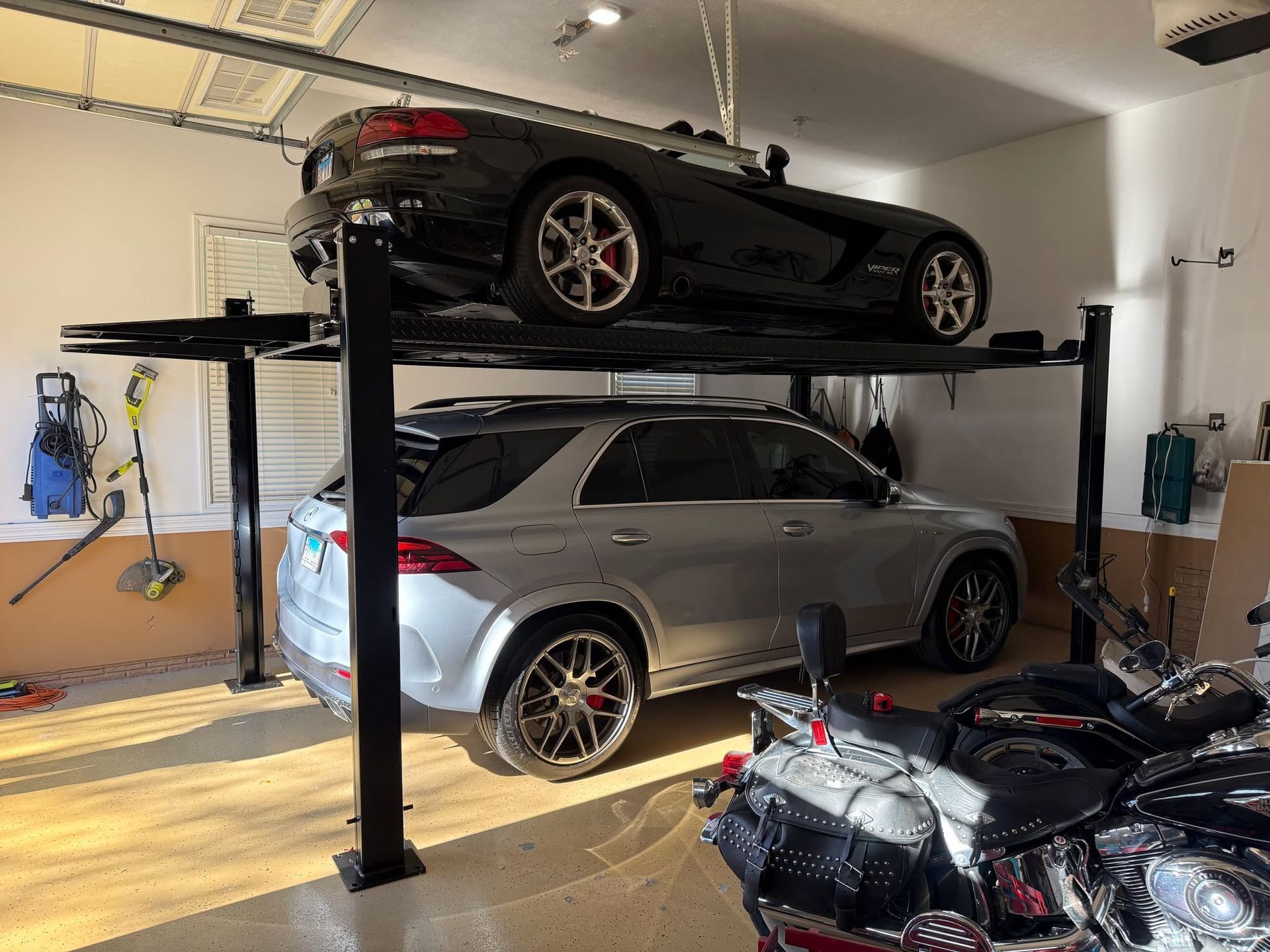 Two cars in a garage, a black sports car parked on a lift above a silver SUV.