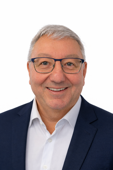 A smiling person wearing glasses, a white collared shirt, and a dark blue blazer against a plain white background.