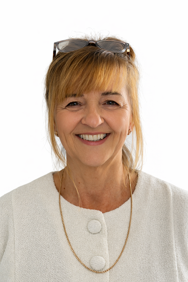 A smiling woman with blonde hair, wearing a white textured top, glasses on her head, and a thin gold chain necklace.