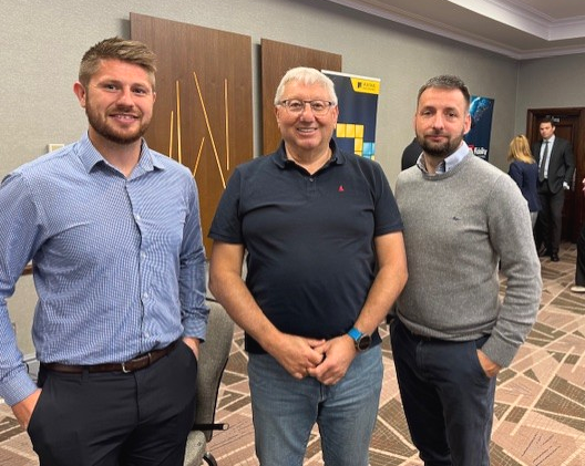 Three men standing together in a hotel hallway, smiling at the camera.
