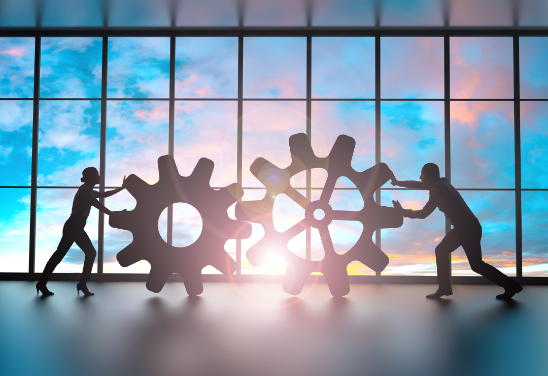 two people backlit, pushing large gears