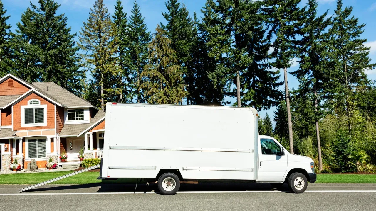 A white box truck parked on the curb near a house with a moving ramp down