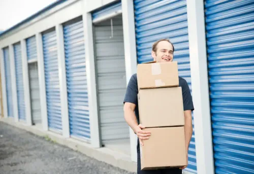 A man carrying boxes next to a bunch of storage units