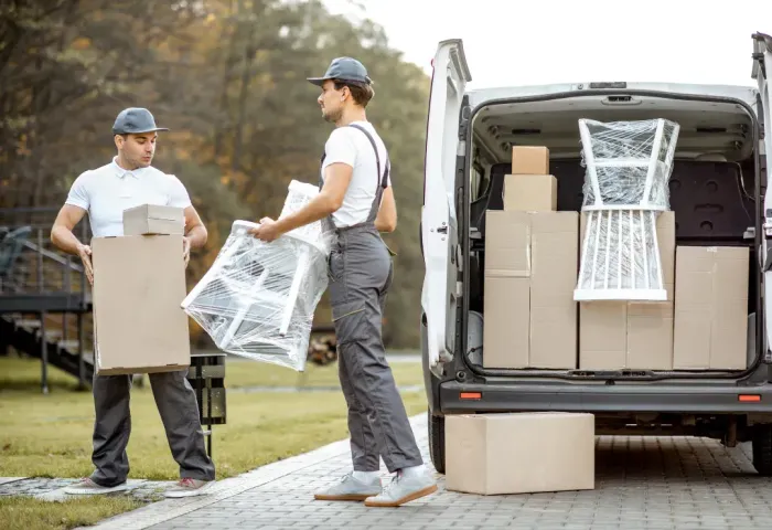 Two men carrying boxes and chairs out of a sprinter van packed with them