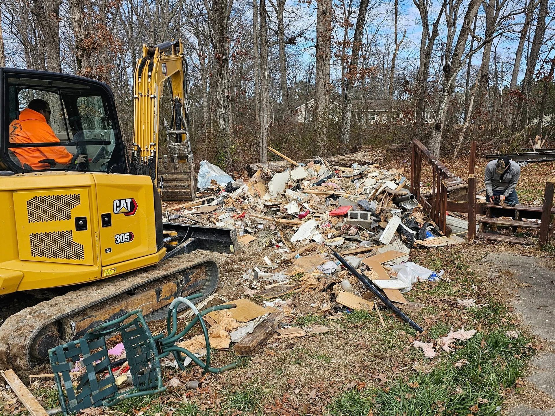 Yellow excavator at a demolition site, a worker operating it, and another person at the debris.