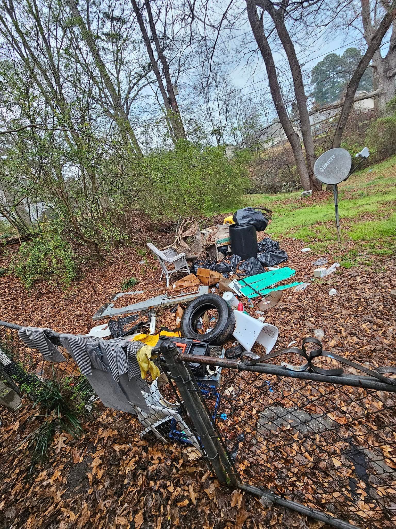 Litter and debris scattered outdoors on a brown leafy surface, near trees and a satellite dish.