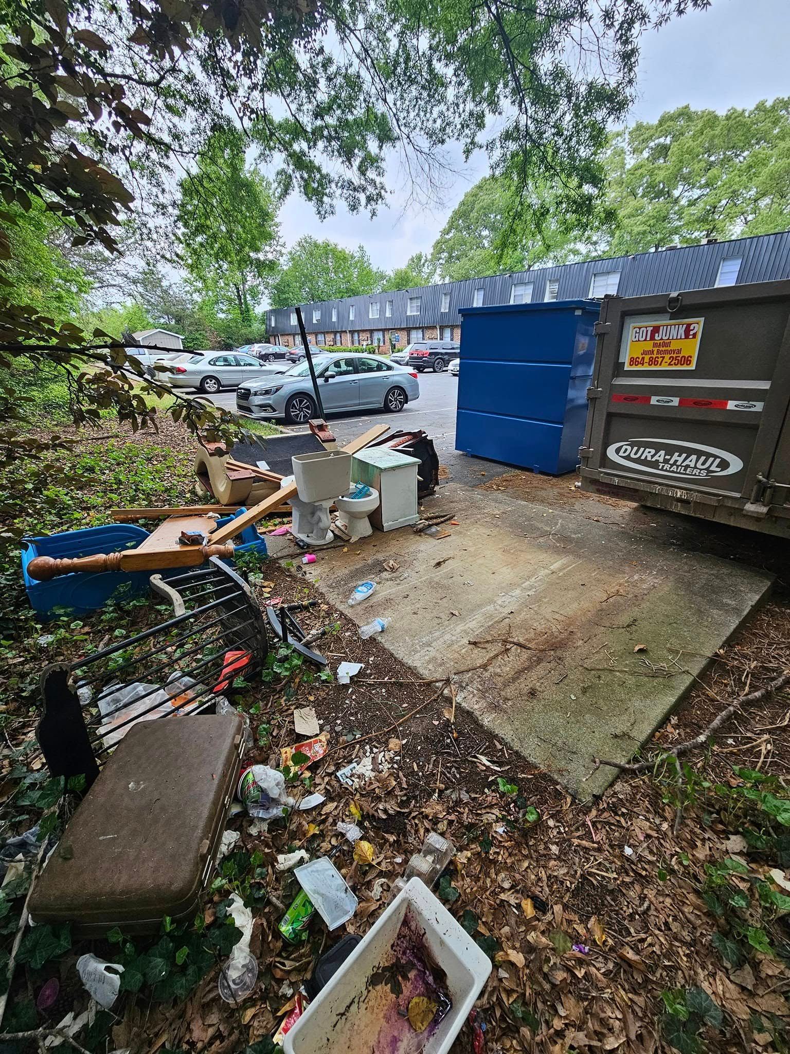 Outdoor scene with overflowing trash near dumpsters. Debris includes a toilet, bathtub and other waste in a residential area.