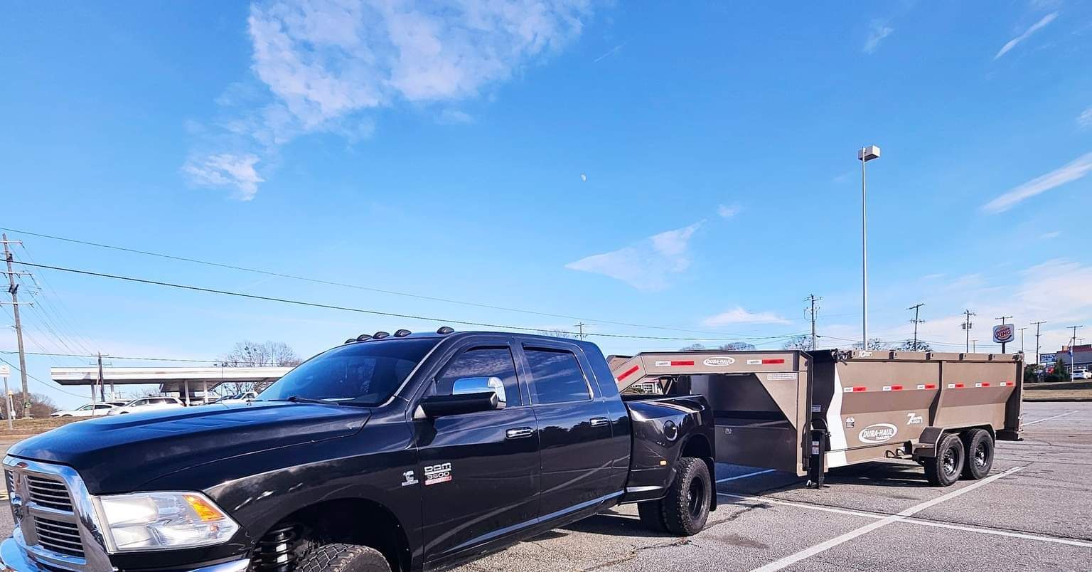 Black pickup truck towing a trailer in a parking lot under a bright blue sky.