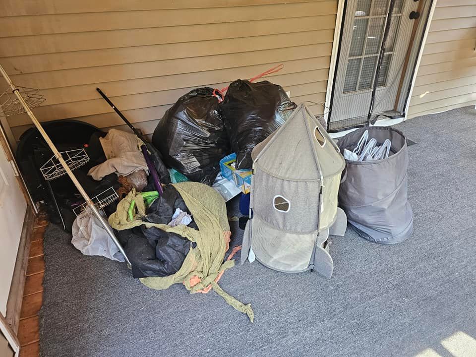 Pile of trash bags, toys, and yard waste on a porch next to a door.