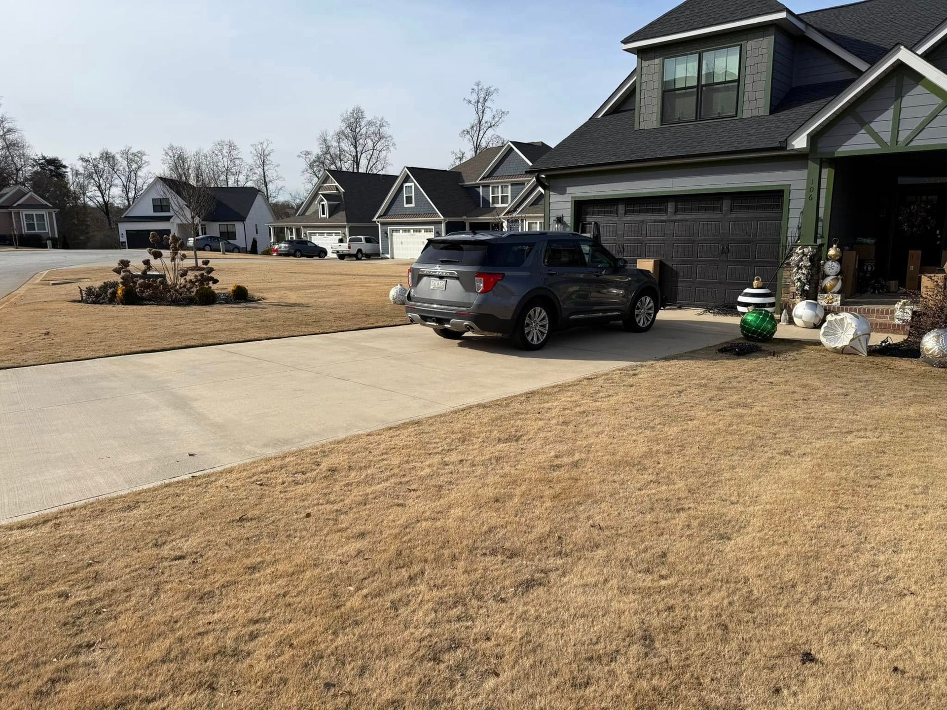 Gray SUV parked in a driveway of a suburban house with a brown lawn and other houses visible.