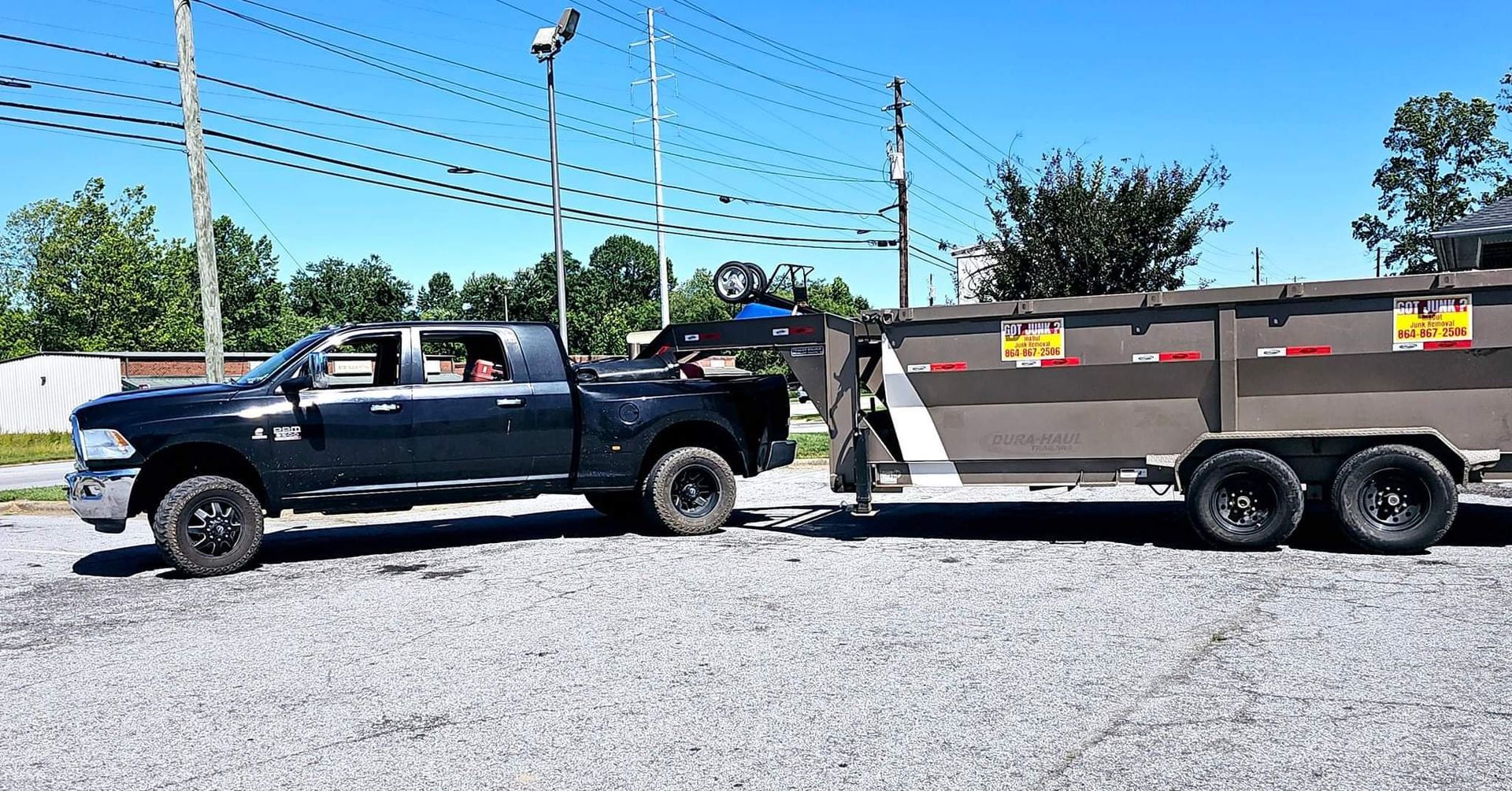Dark truck towing a dump trailer on a gravel surface. Bright sunny day.