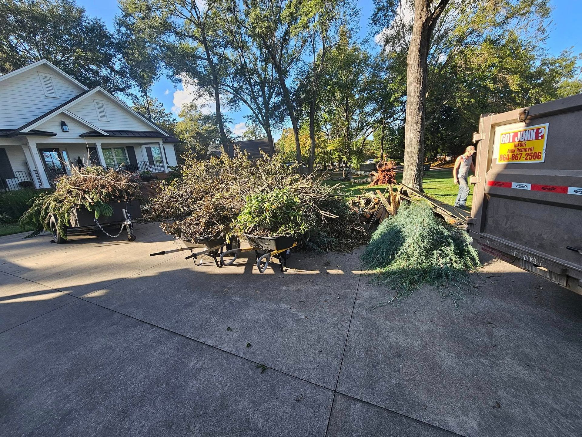 Debris from tree trimming on a driveway next to a house, being loaded into a garbage truck.