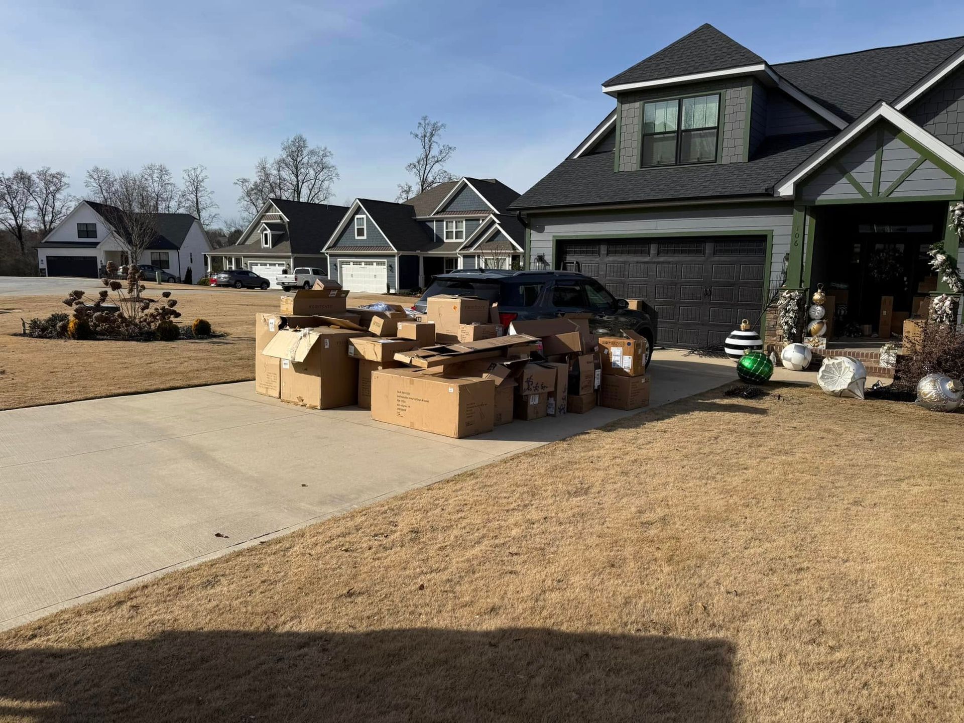 Cardboard boxes piled in a driveway next to a black garage; a house in a residential neighborhood.