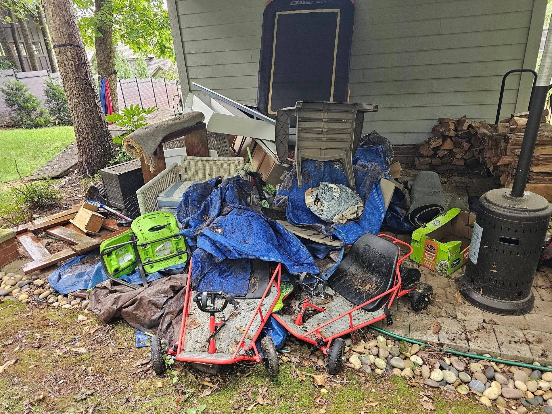 Pile of trash outside: two go-karts, blue tarp, old heater, boxes, and other debris.