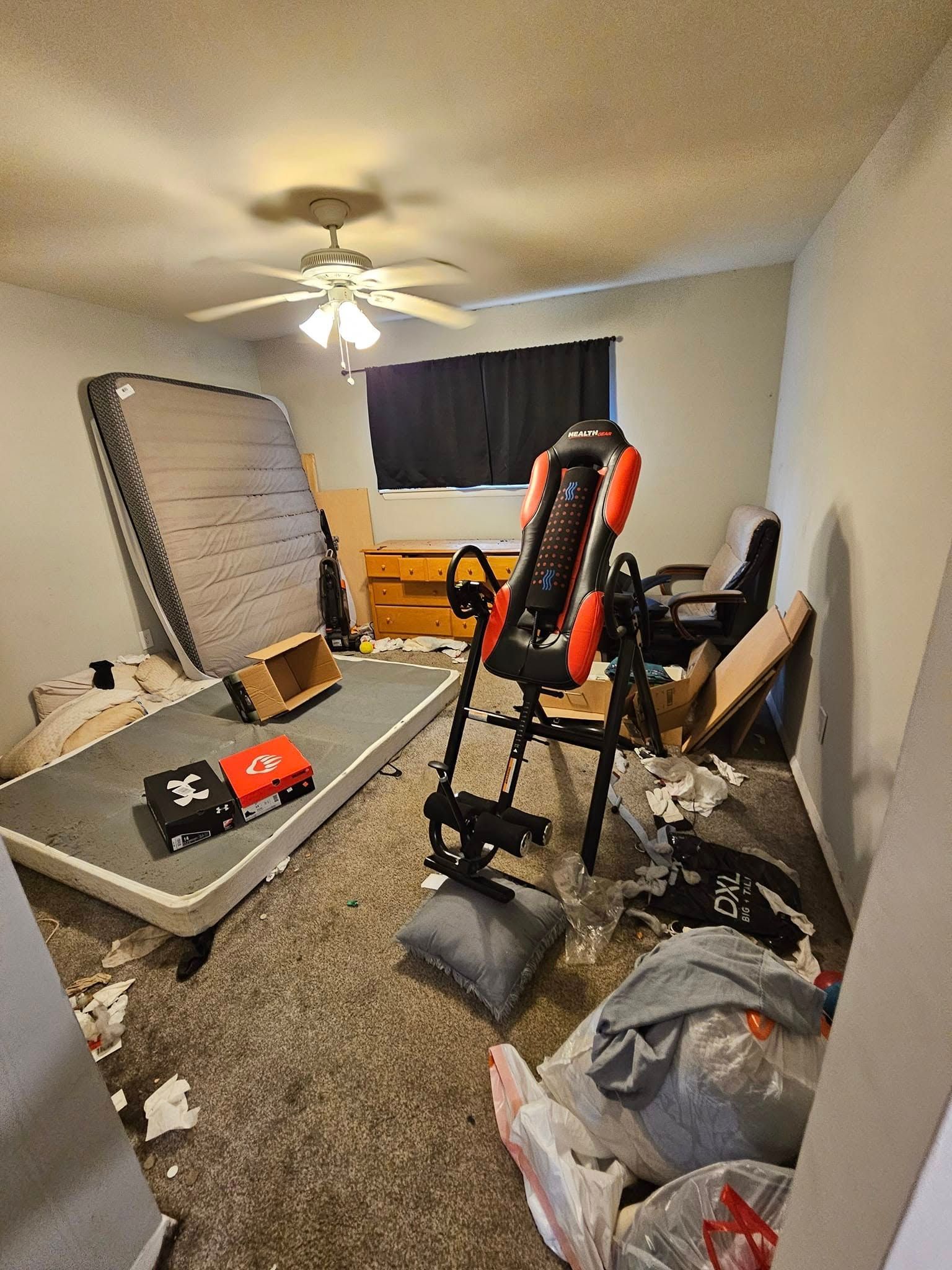 A messy bedroom with an exercise machine, mattress, and trash scattered on the floor.