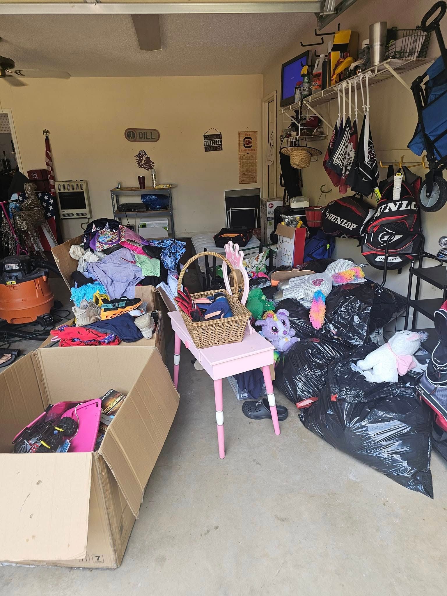 A garage sale with clothing, bags, and a small table in a cluttered garage.
