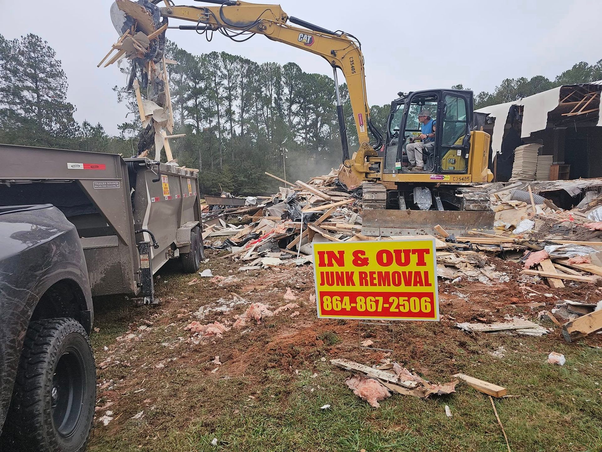 Demolition site: Yellow excavator tears down a structure, loading debris into a truck. Sign: 