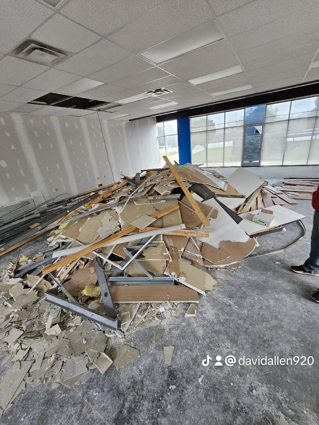 Pile of construction debris on the floor of a room under renovation, ceiling partially open, daylight coming in.