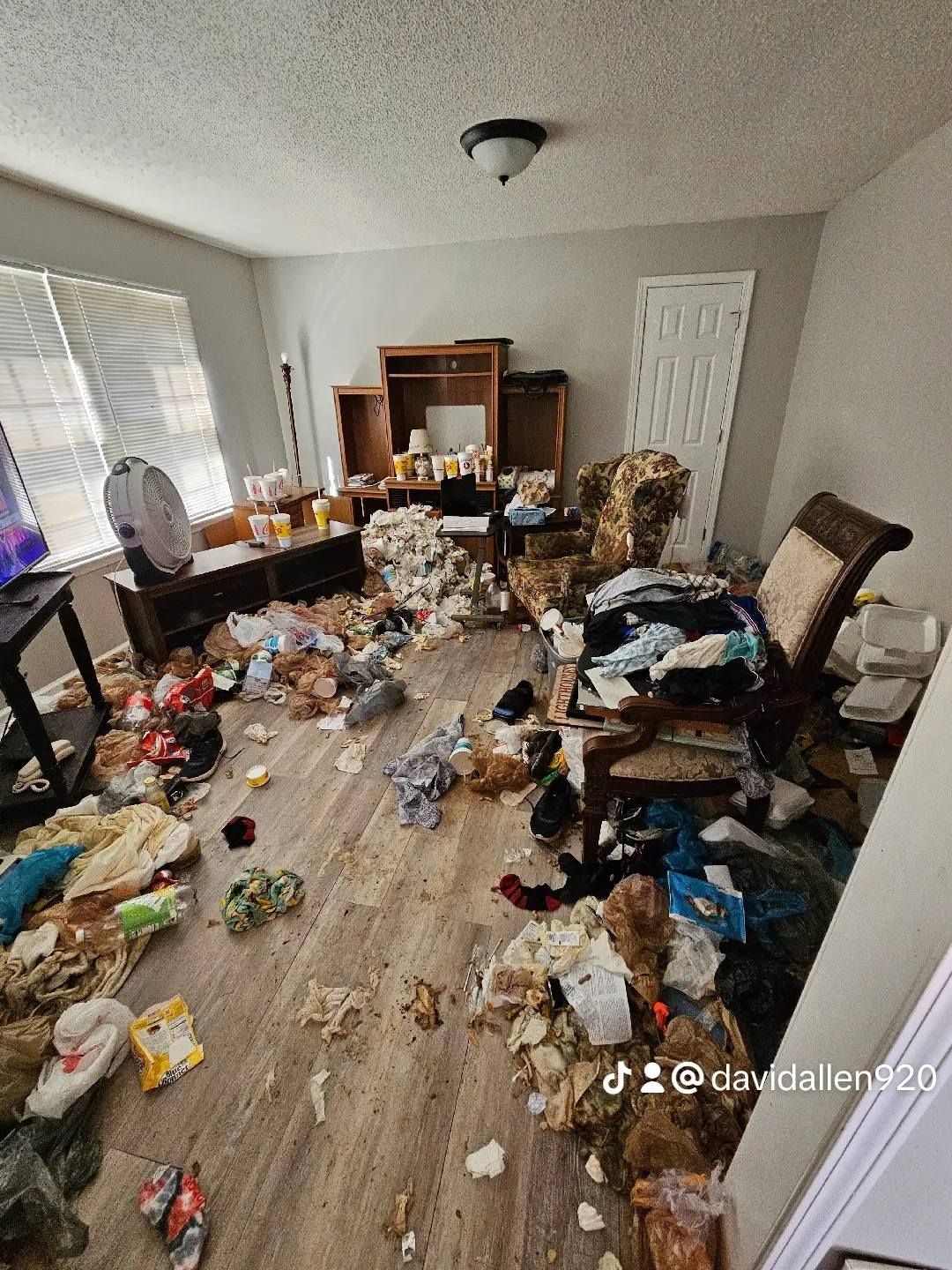 Messy room with debris on the floor, furniture obscured by clutter. Beige walls, sunlight through window.