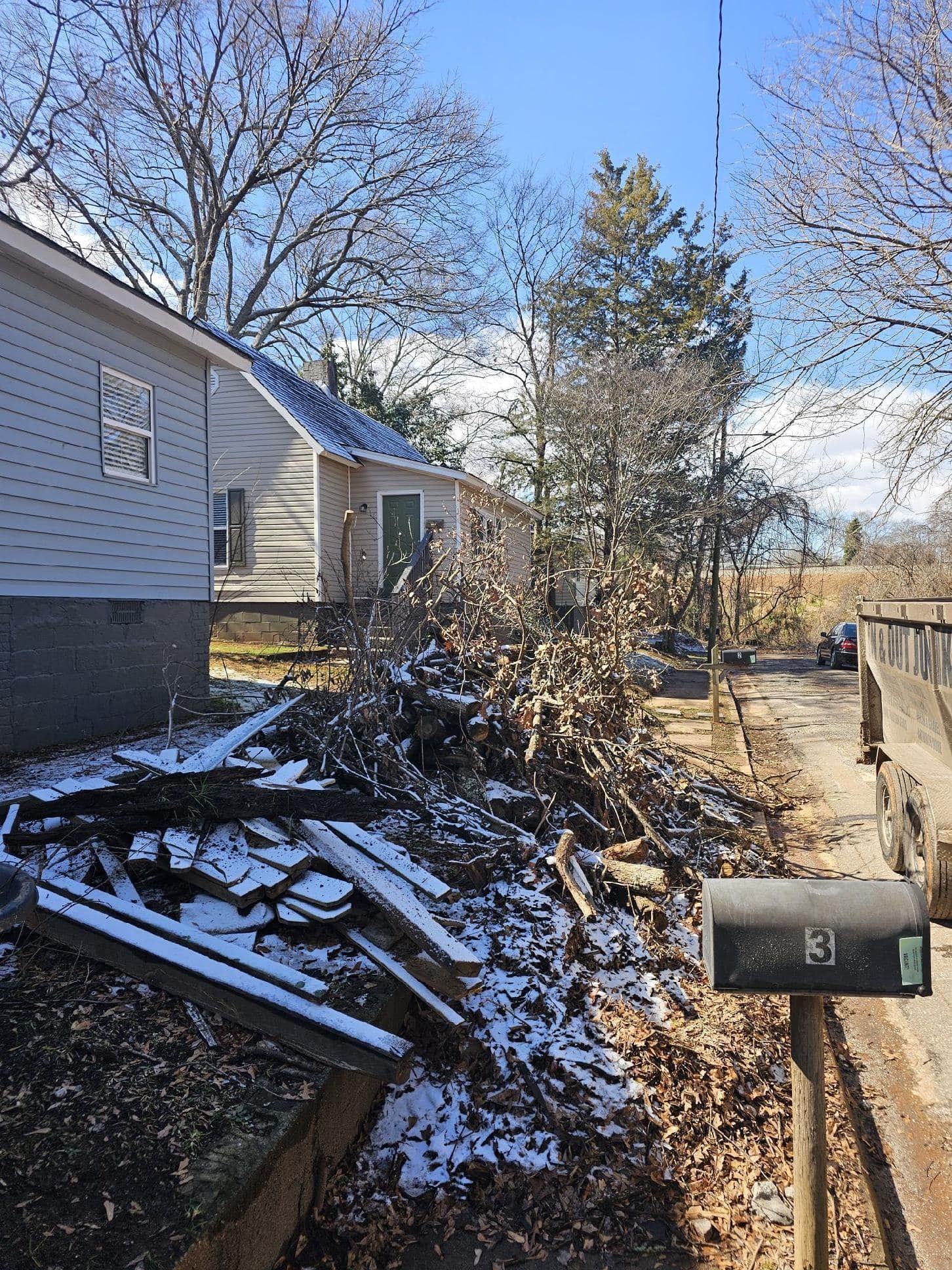 Snowy debris pile next to houses with a mailbox on a pole.