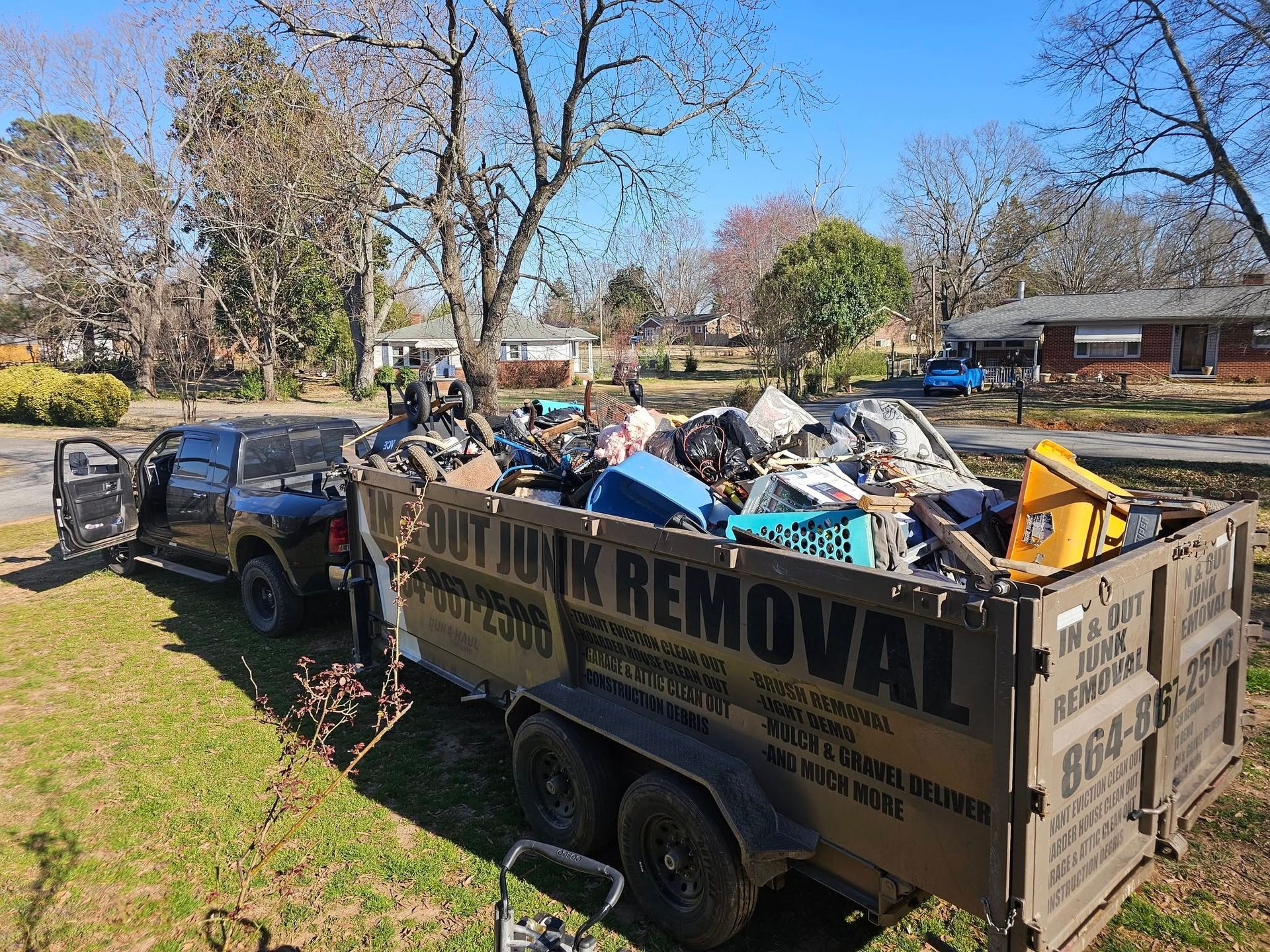 A truck hauls a trailer filled with junk. Sunny residential street.