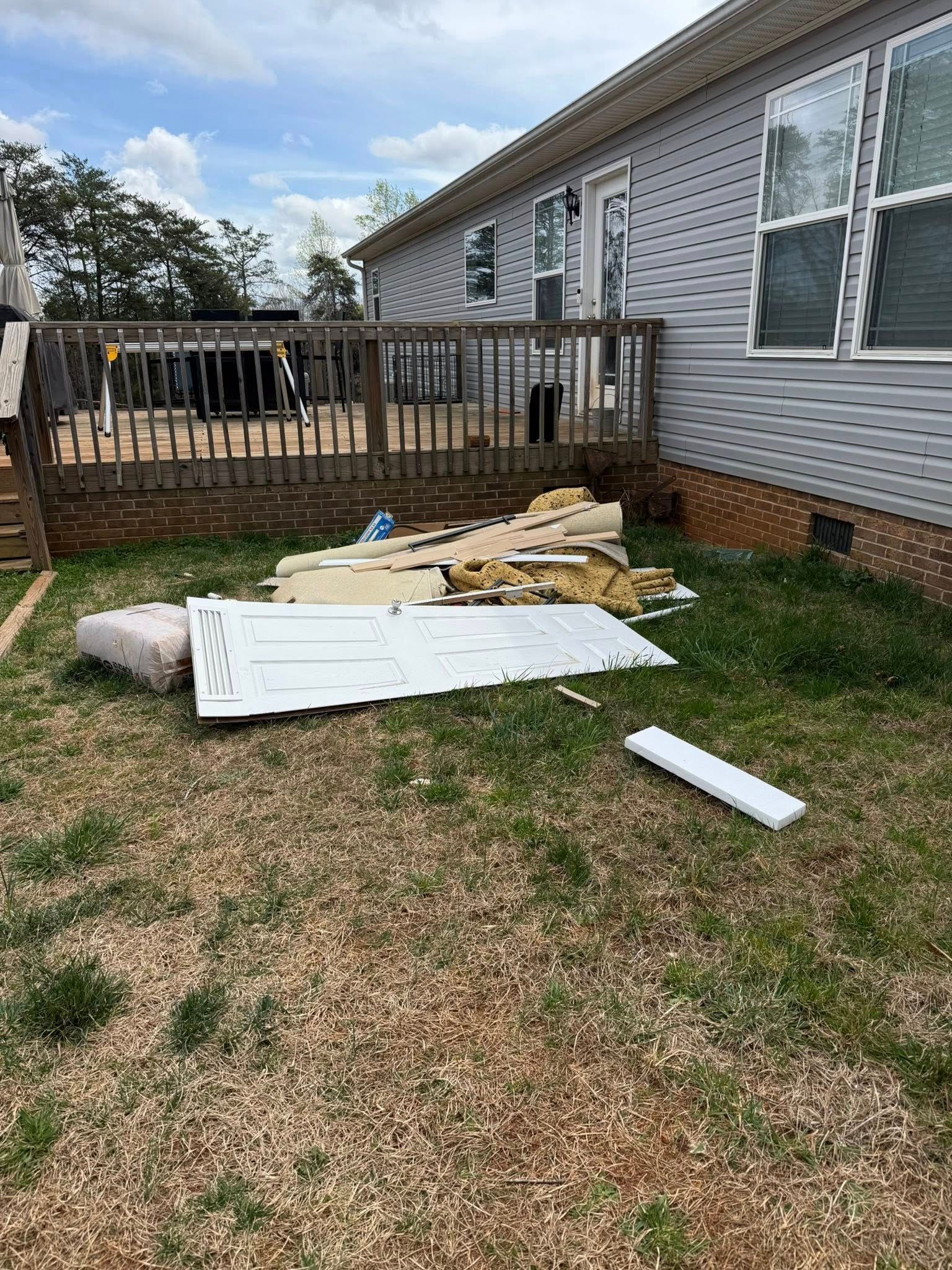 Pile of construction debris in a grassy backyard next to a house with a wooden deck.