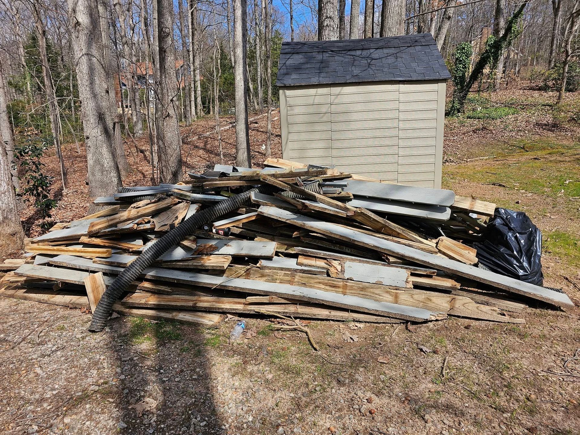 Pile of weathered wood debris in a yard, with a small shed in the background.