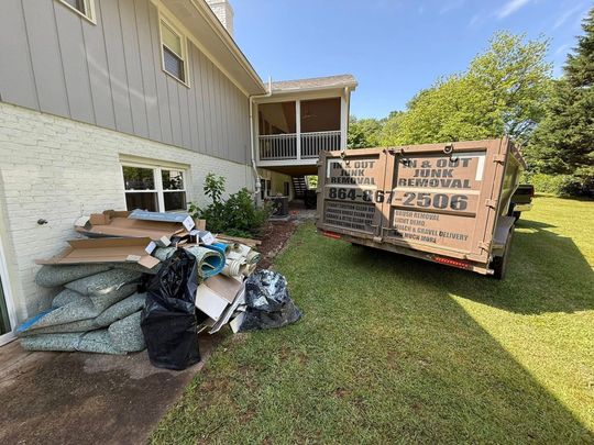 Pile of trash in front of a light-colored building, with trees in the background under a blue sky.