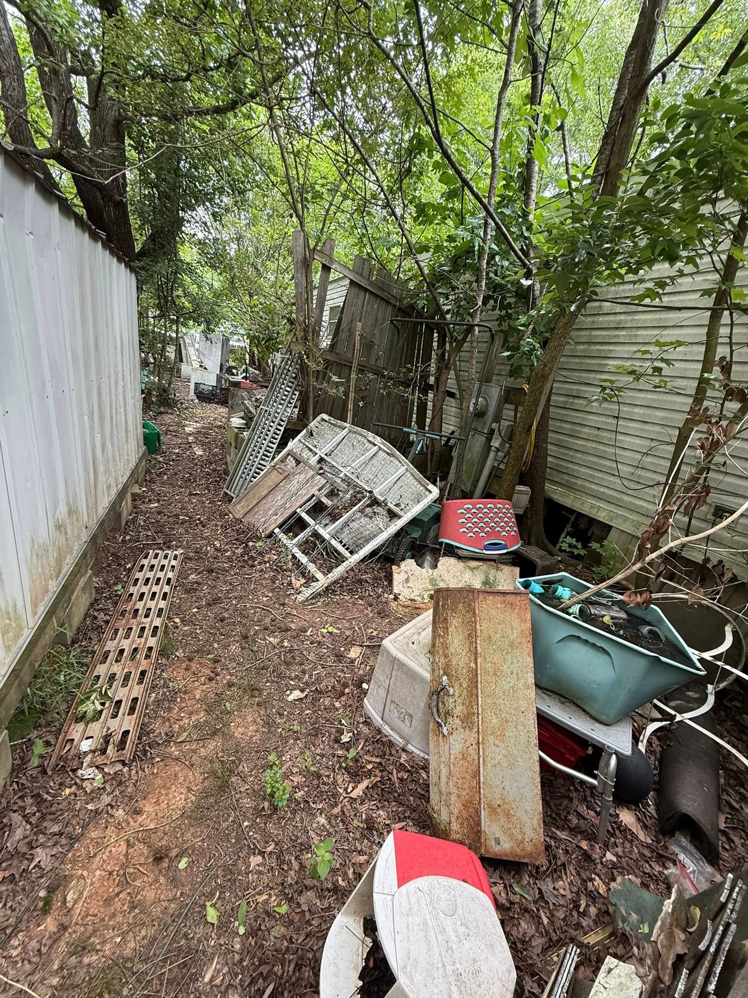 Backyard littered with debris, overgrown with trees. White siding on left.
