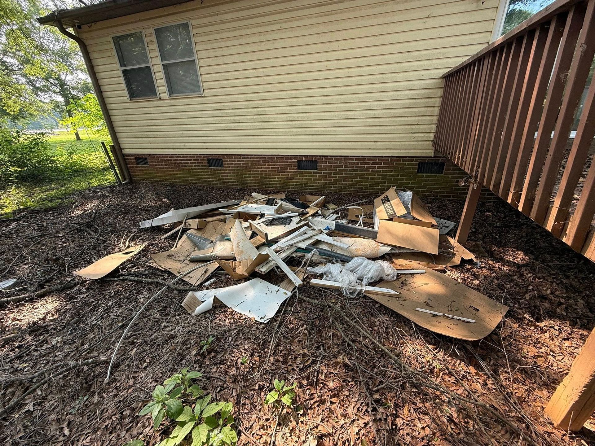 Pile of debris and cardboard boxes by a house with a brown deck.