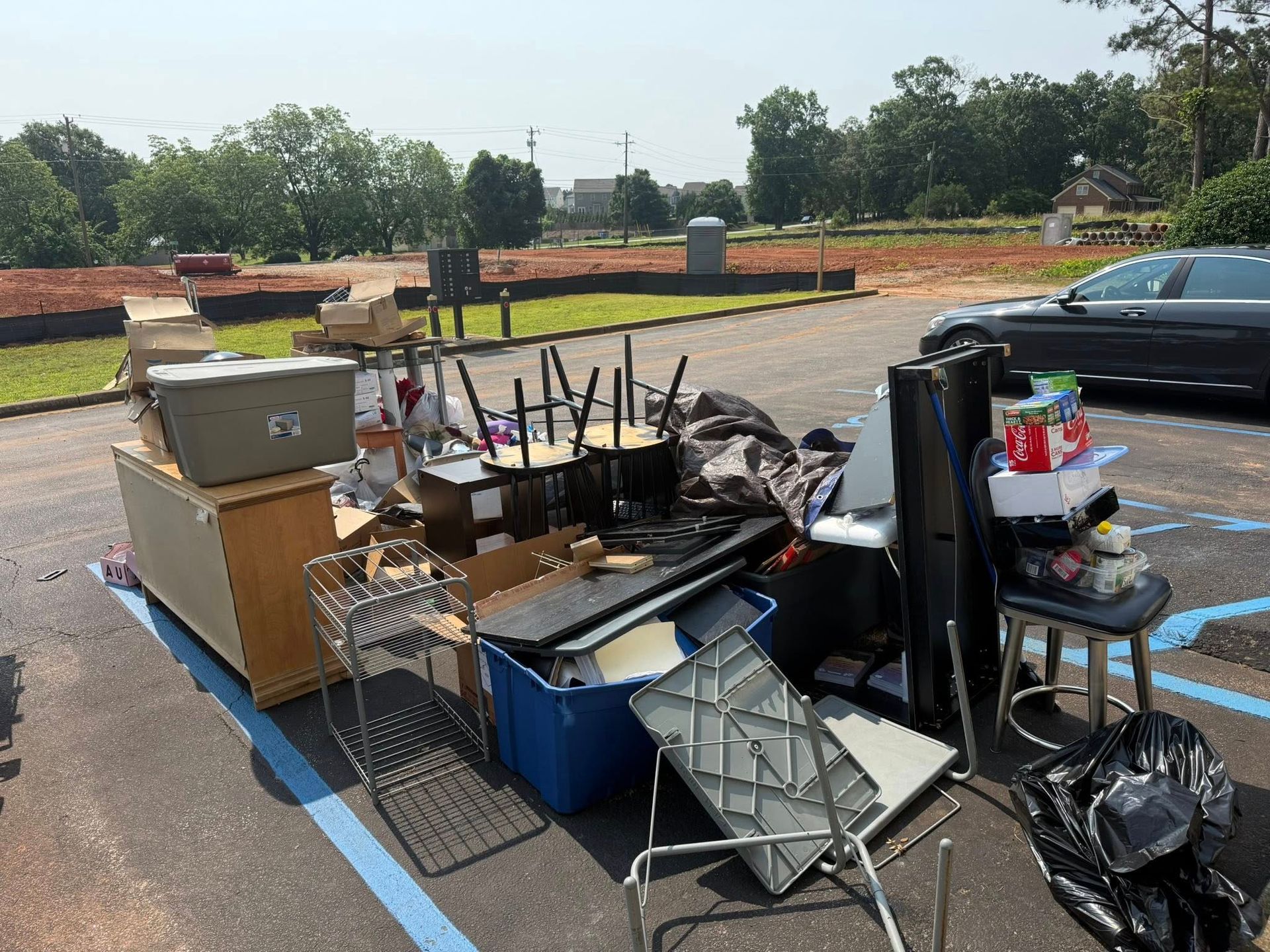 Pile of discarded furniture and items in a parking lot, including chairs, a cabinet, and boxes, on a sunny day.