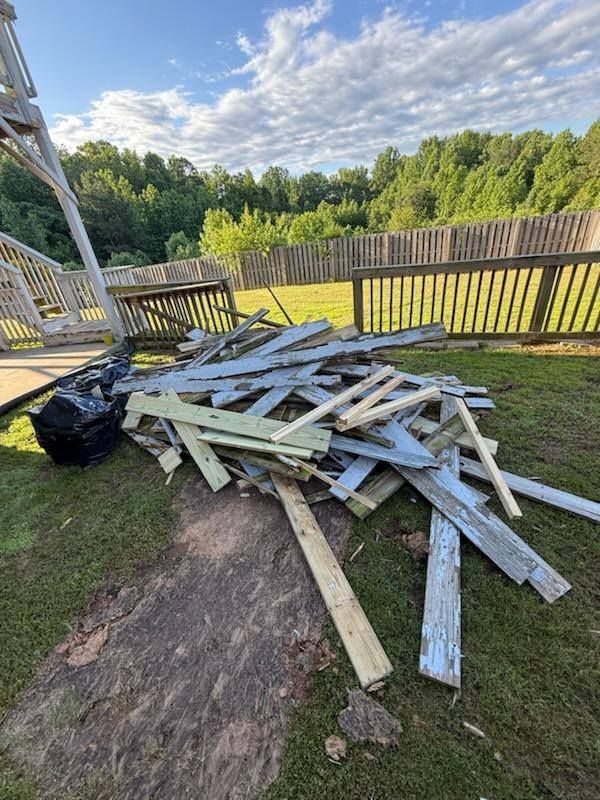 Pile of weathered, painted wood scraps on grass, near a deck and fence in a backyard.