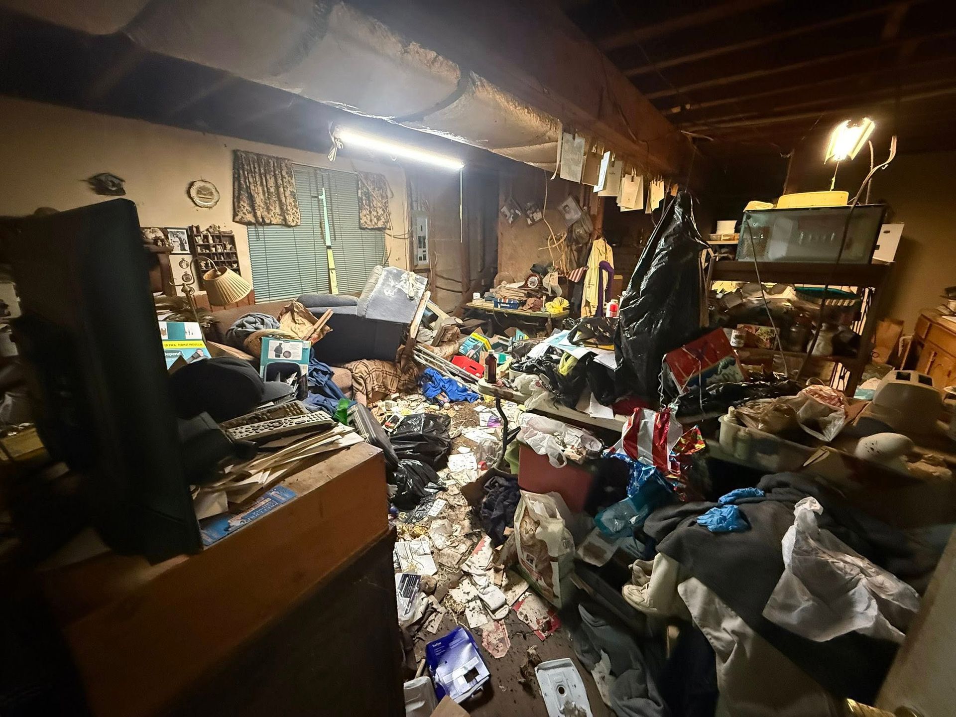 Cluttered basement, filled with trash and disorganized items. Dim lighting, various objects on shelves and floor.