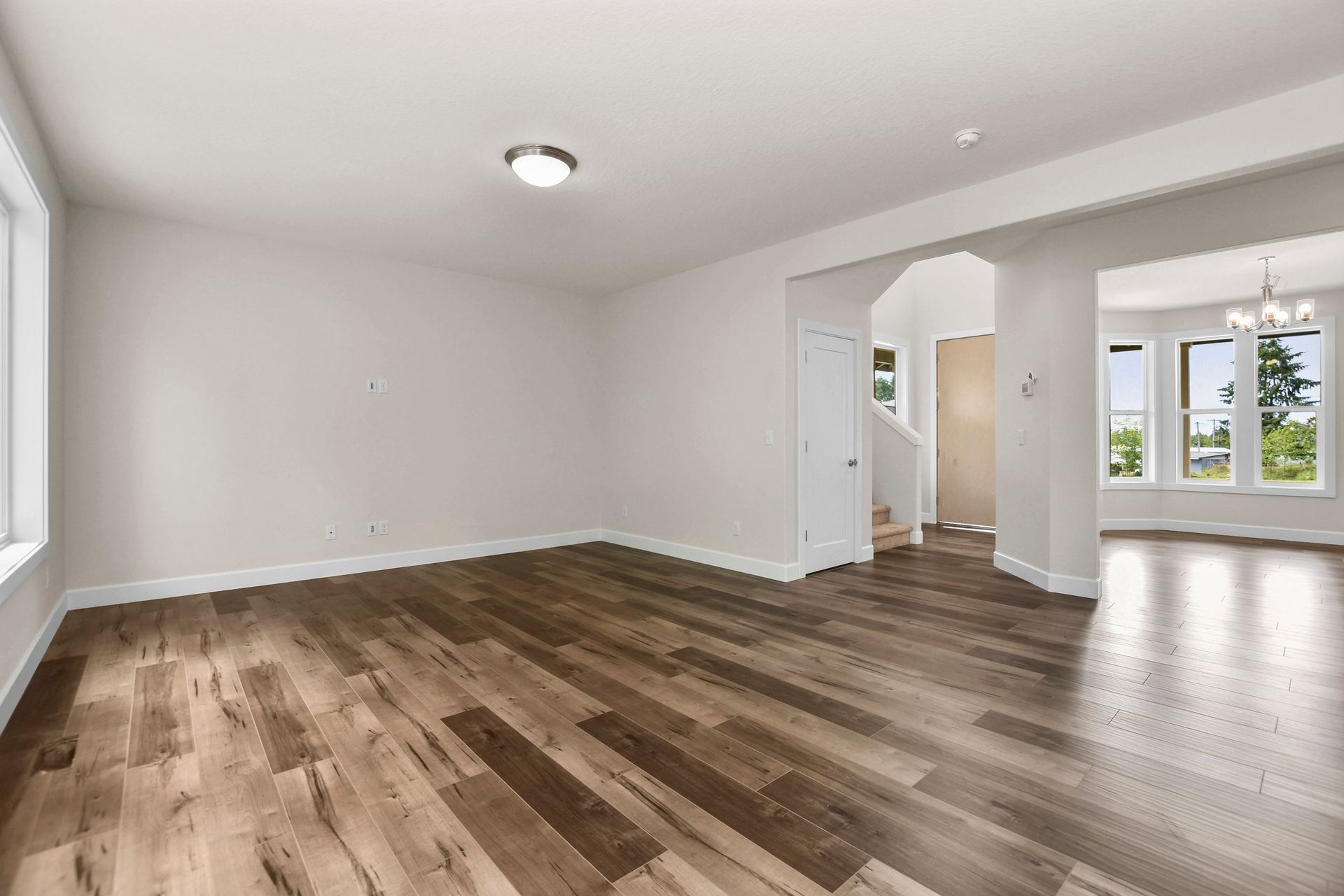Empty living room with wood floors, white walls, and an arched opening to a bright adjoining room.